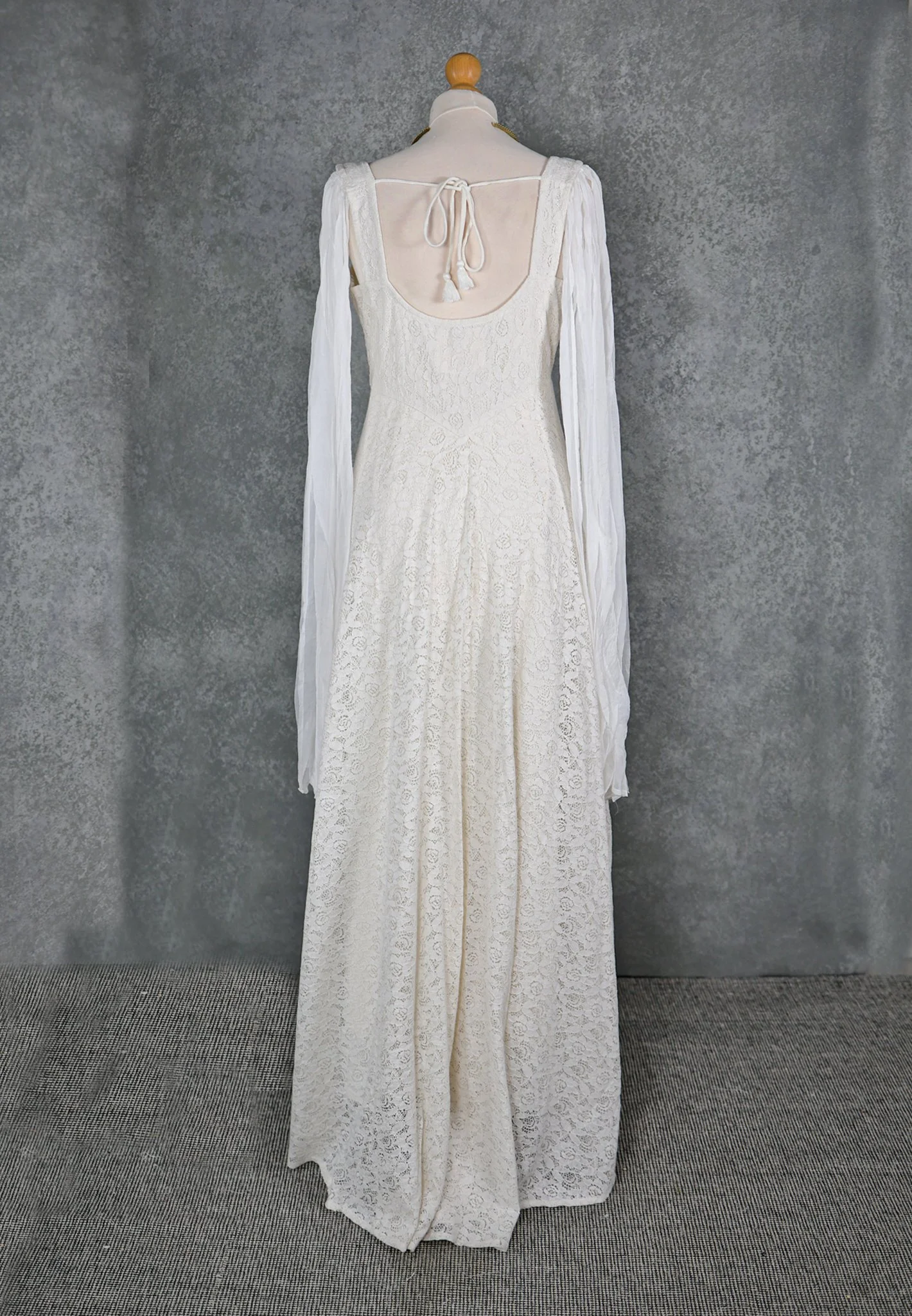 The Lir Wedding Dress, a Celtic-inspired Irish bridal gown featuring ivory lace over linen, a ribboned corset bodice, and detachable sheer sleeves tied with tassels for romantic styling options.