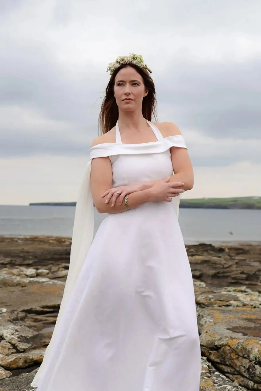 White halterneck linen wedding dress with off-shoulder wrap and flowing chiffon sleeves. Figure-hugging fit with full skirt, sustainably made and perfect for Celtic-inspired ceremonies.