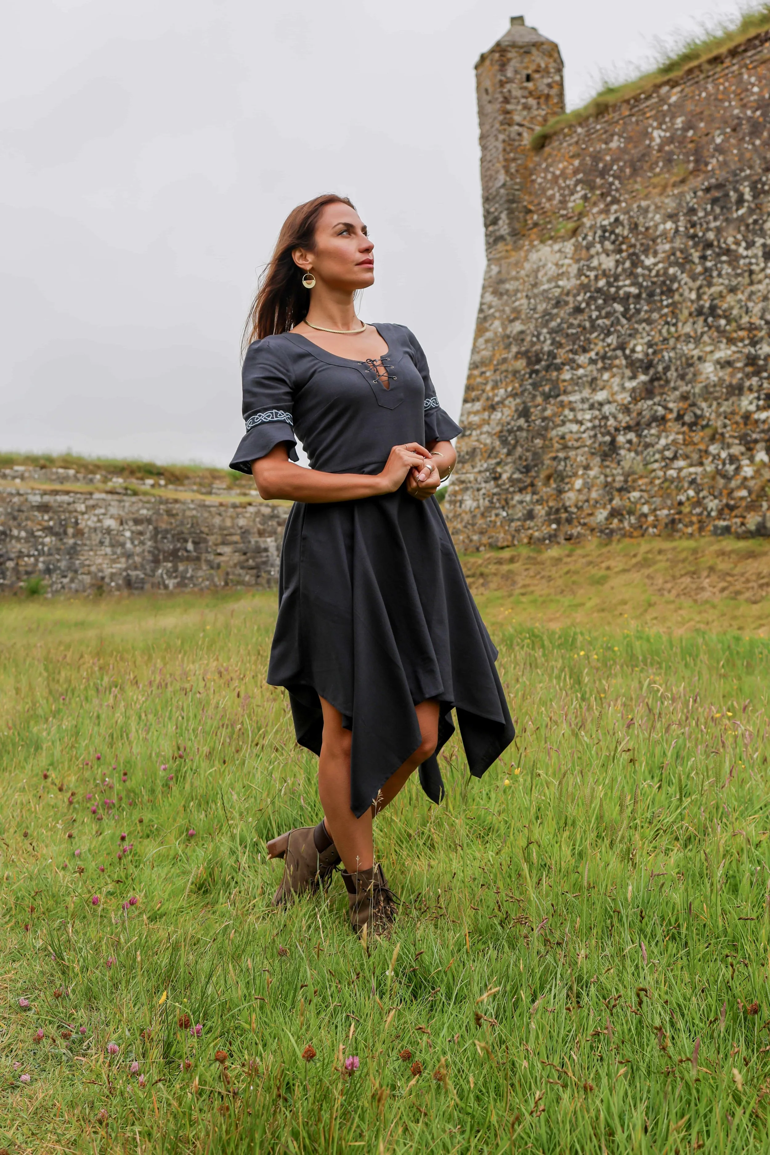 Model wears a blue corset dress with Celtic embroidery and flowing handkerchief skirt, styled as a Celtic dress with pockets.