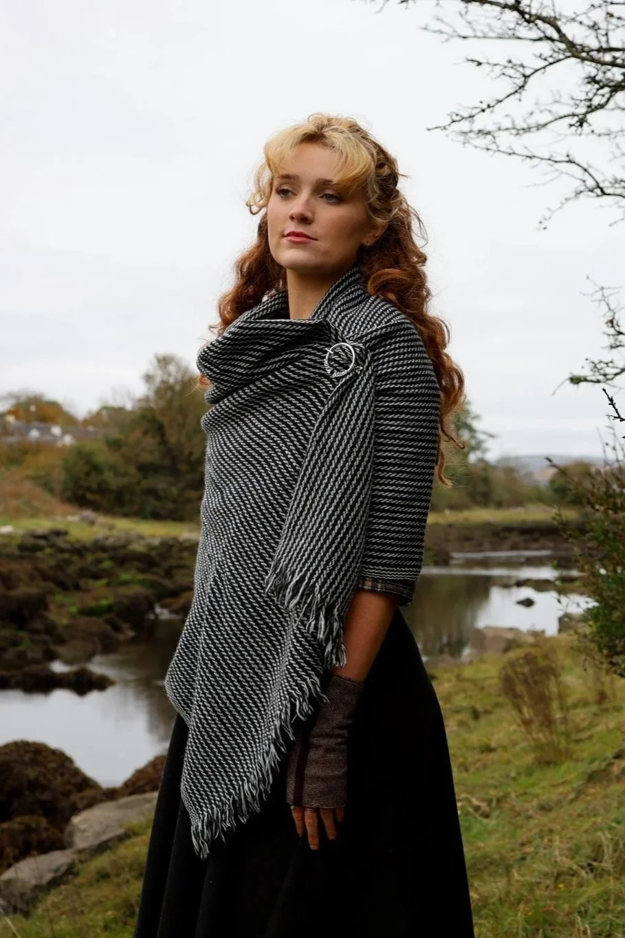 Model wearing a handwoven black and grey Celtic shawl secured with a silver-plated Trinity Knot brooch by Celtic Fusion Design. Photographed in the Irish countryside