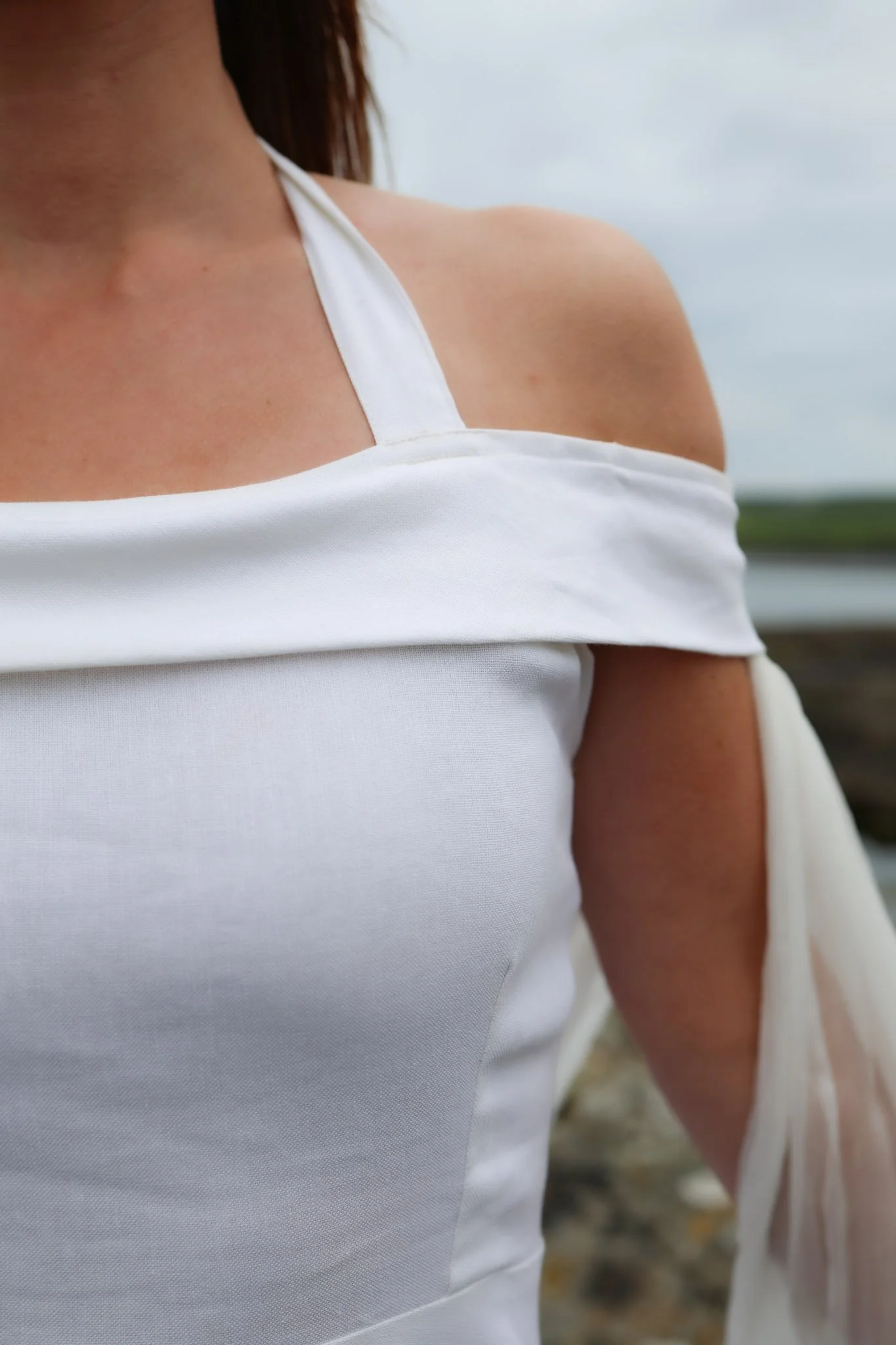 white linen halter neck wedding dress with off-shoulder wrap and chiffon sleeves, shown on Irish coastal rocks with close-up of structured bodice.