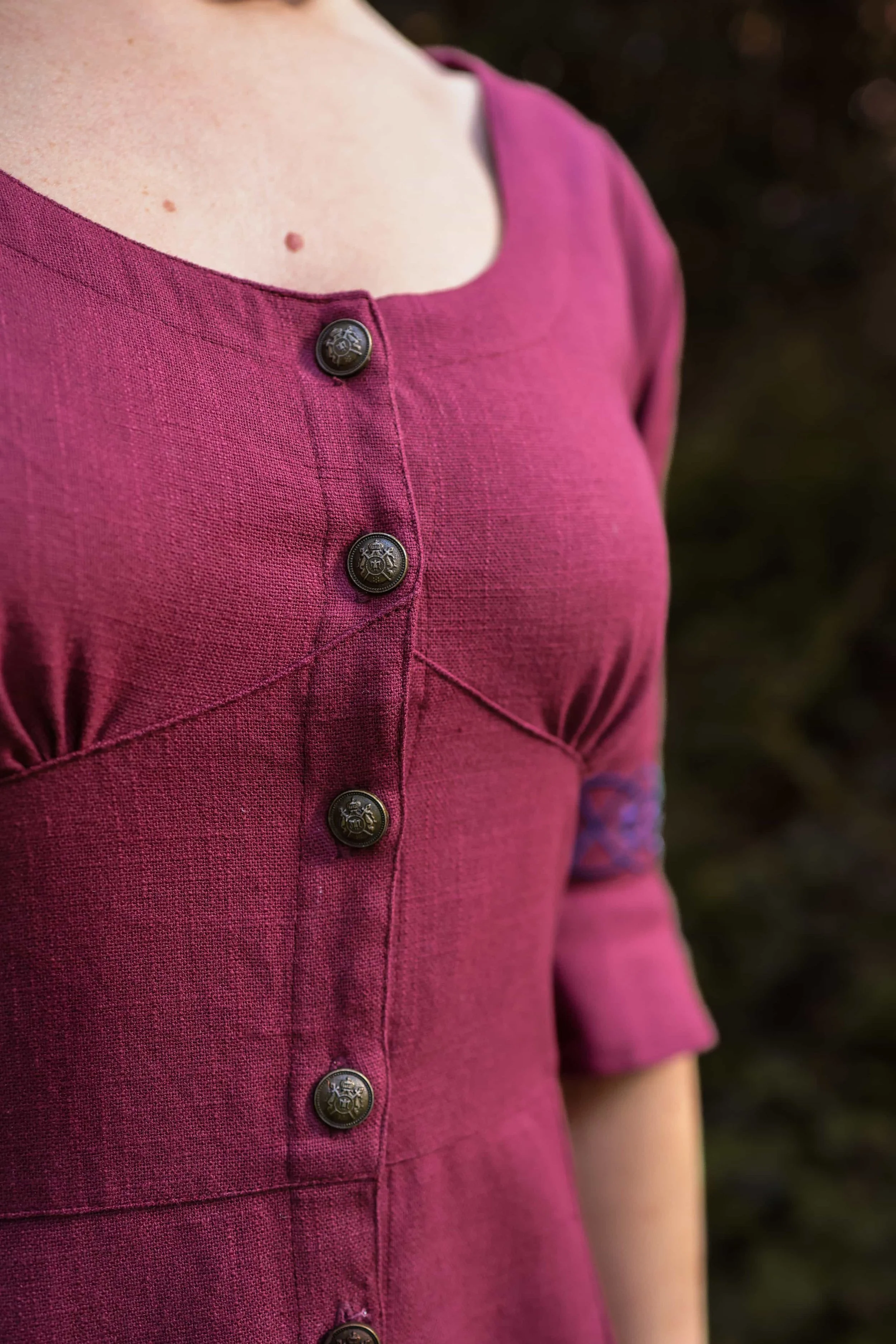 Model wearing a deep berry red Celtic dress with Celtic knot embroidery, button-down front, and flowing sleeves – Pooka Hawthorn Dress by Celtic Fusion Design