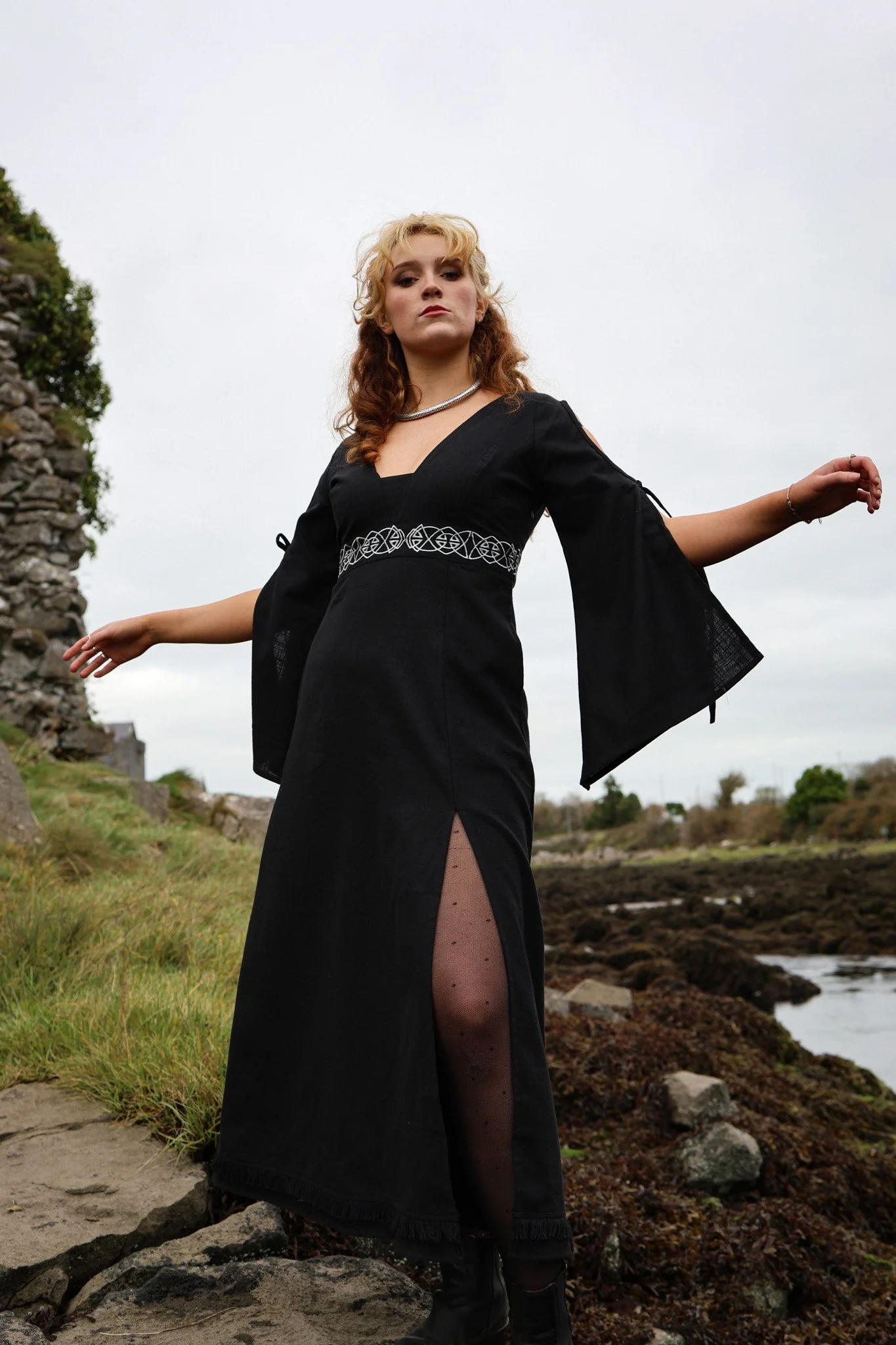 Model wearing a Black Celtic dress with Celtic knot embroidery, styled in a medieval stone ruin.