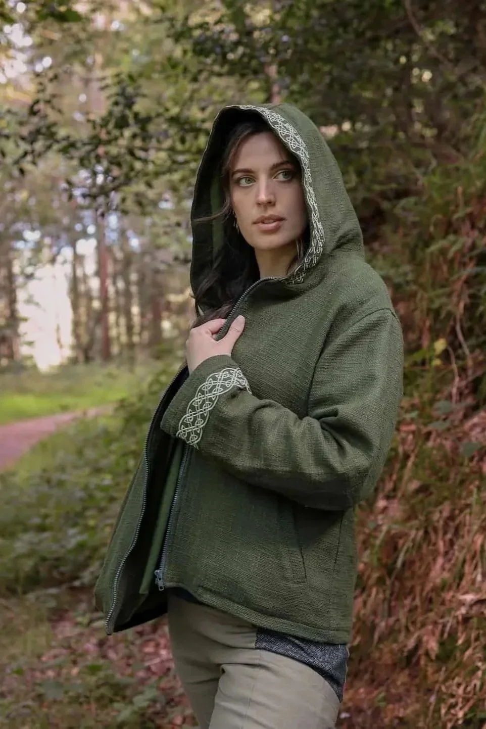 A woman wears the moss green Hooded Jacket with Fleece Lining and Embroidered Celtic Knotwork