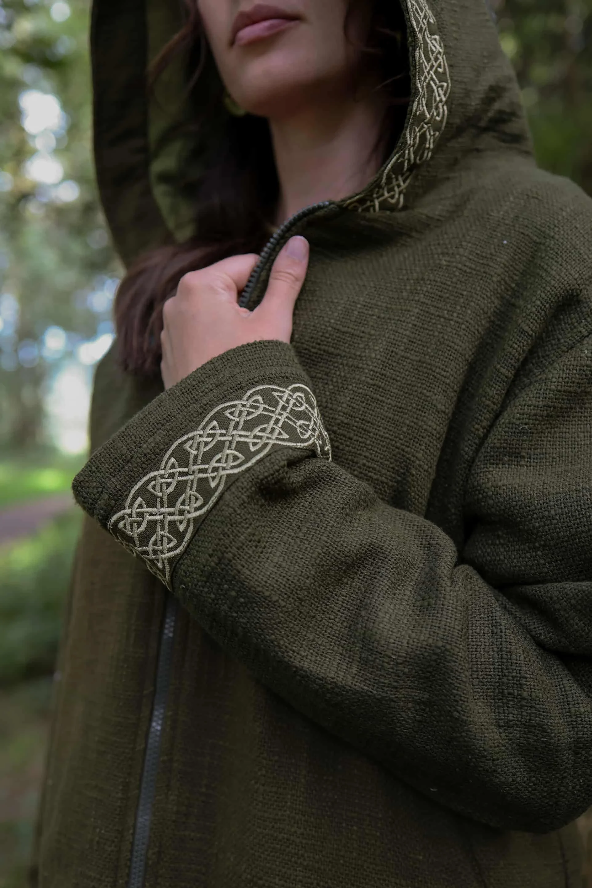 A woman wears the moss green Hooded Jacket with Fleece Lining and Embroidered Celtic Knotwork