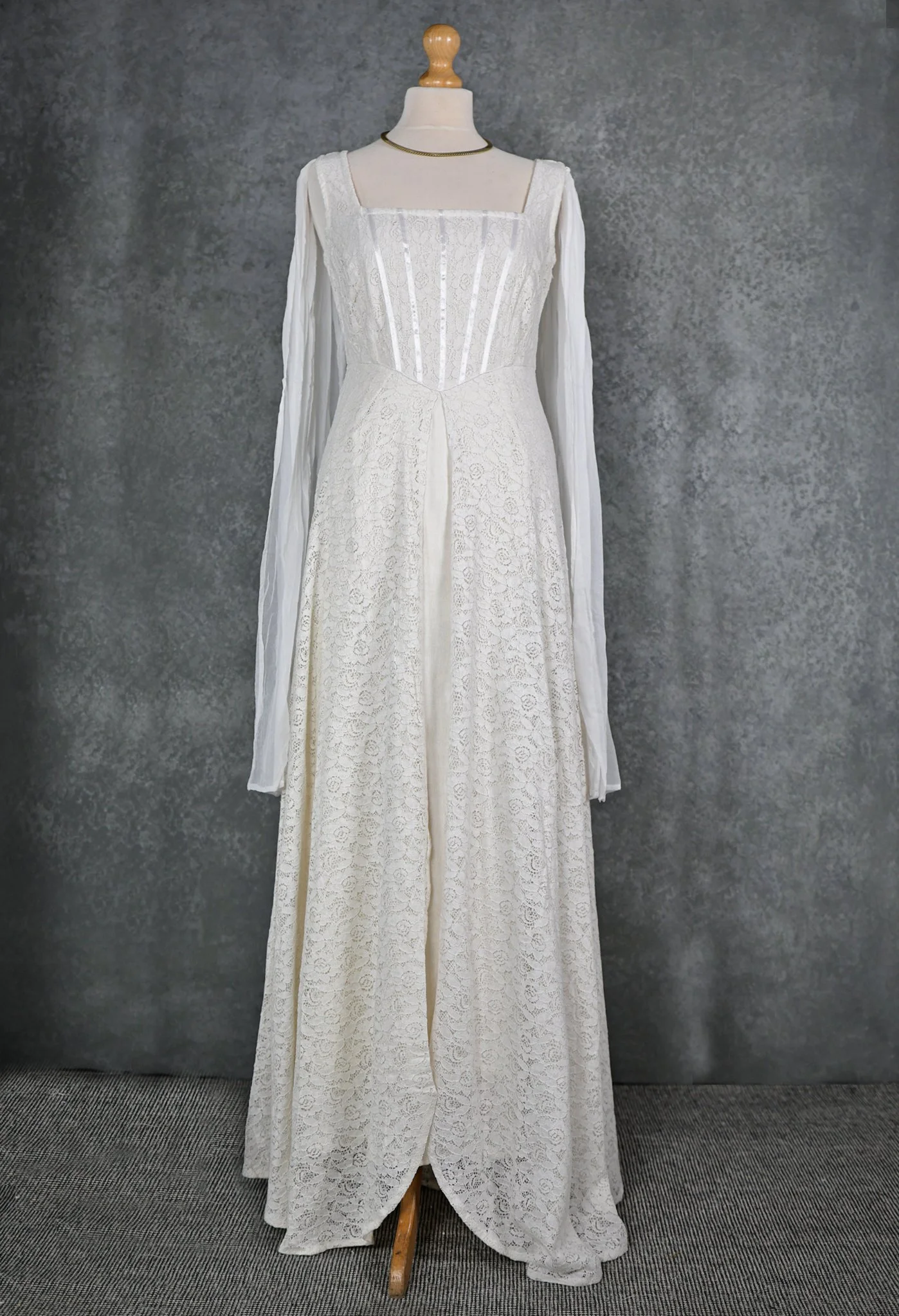The Lir Wedding Dress, a Celtic-inspired Irish bridal gown featuring ivory lace over linen, a ribboned corset bodice, and detachable sheer sleeves tied with tassels for romantic styling options.