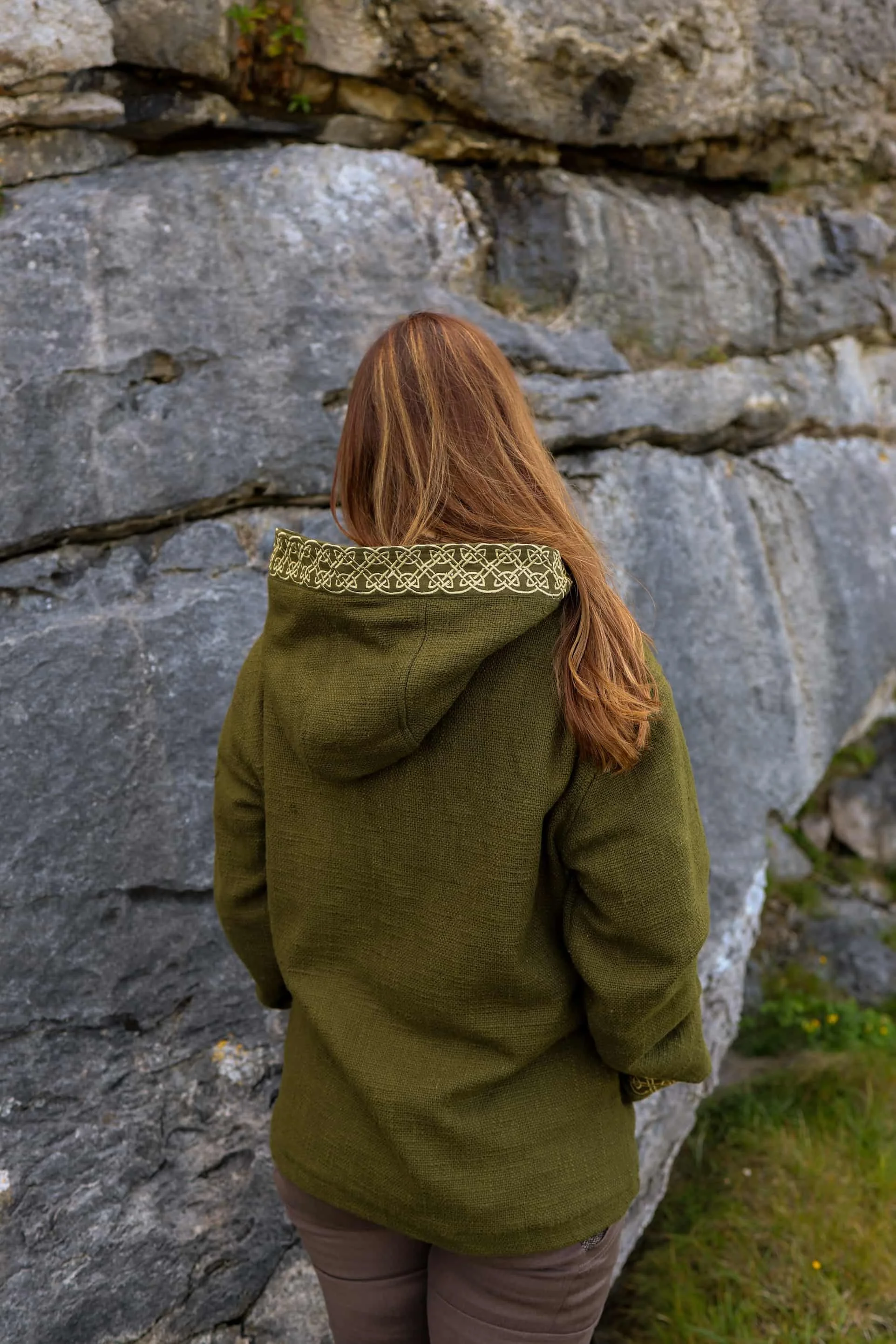 A woman wears the moss green Hooded Jacket with Fleece Lining and Embroidered Celtic Knotwork