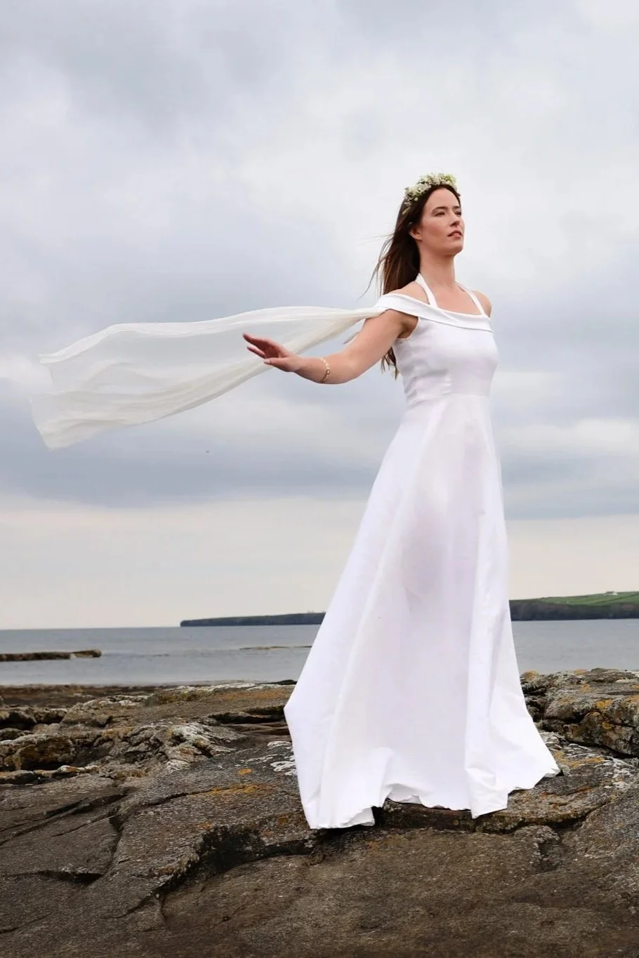 White halterneck linen wedding dress with off-shoulder wrap and flowing chiffon sleeves. Figure-hugging fit with full skirt, sustainably made and perfect for Celtic-inspired ceremonies.