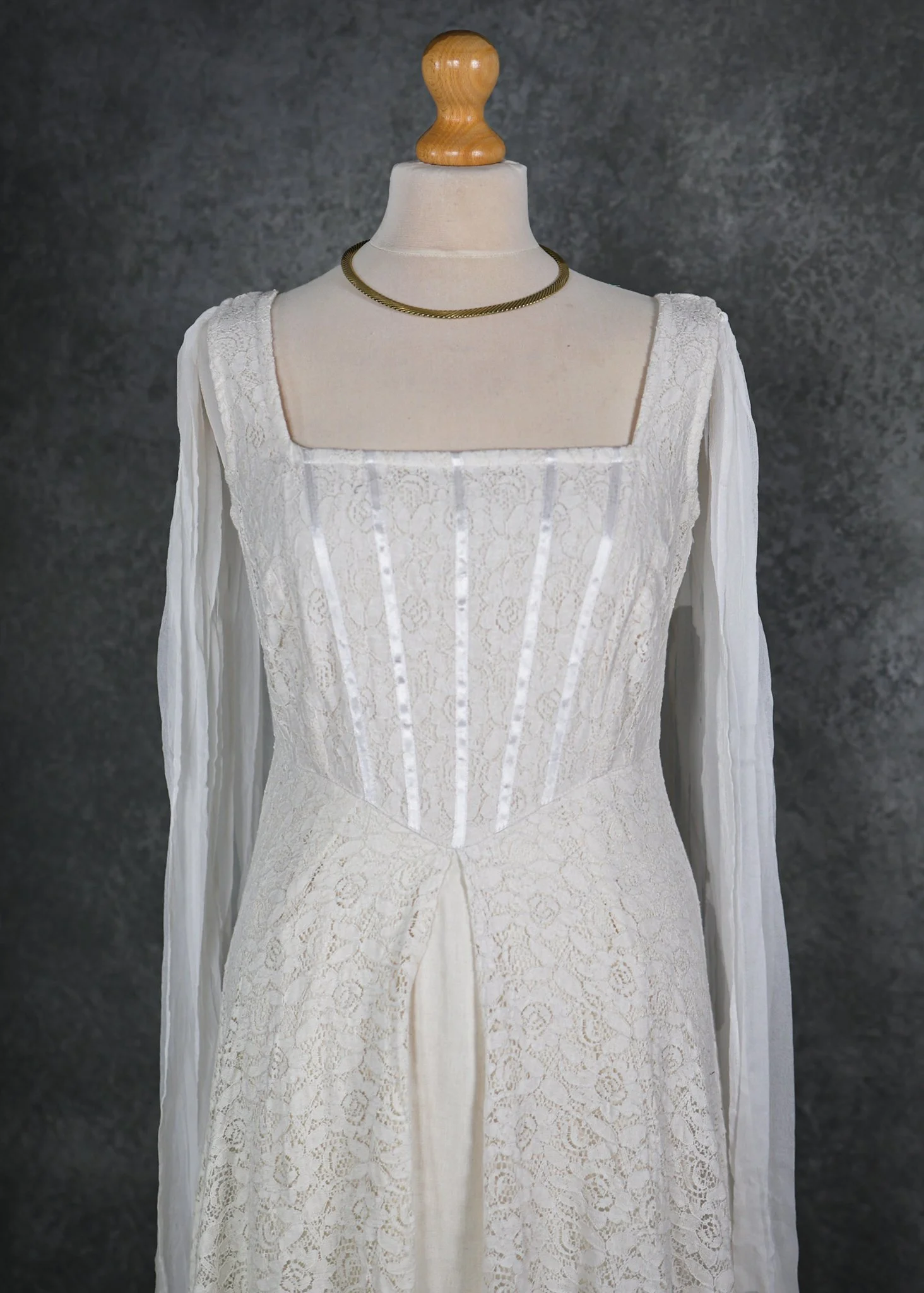 The Lir Wedding Dress, a Celtic-inspired Irish bridal gown featuring ivory lace over linen, a ribboned corset bodice, and detachable sheer sleeves tied with tassels for romantic styling options.