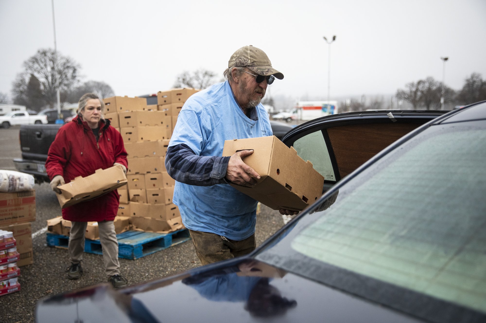  Volunteers Terry Scovil (center), and Shendi Klopfer load the car of a community member with food from the Trinity County Food Bank at the Trinity County Fairgrounds on Feb. 8, 2023. Photo by Martin do Nascimento, CalMatters 