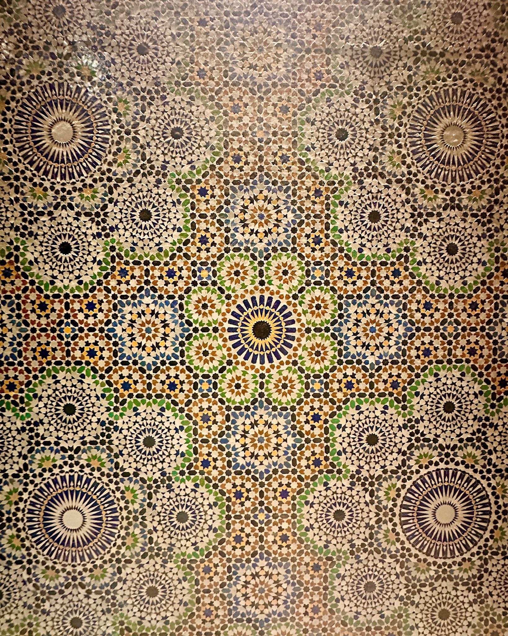 Intricate mosaic tile ceiling with geometric star and floral patterns in earthy tones of brown, green, blue, and cream.