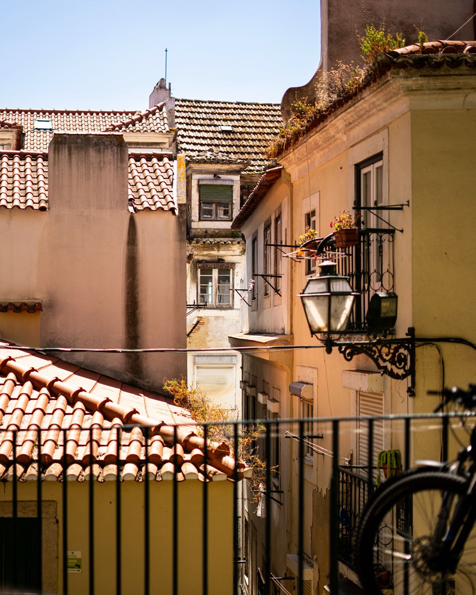 View of old European-style buildings with tiled roofs, windows, balconies, and a street lamp, under a clear blue sky.