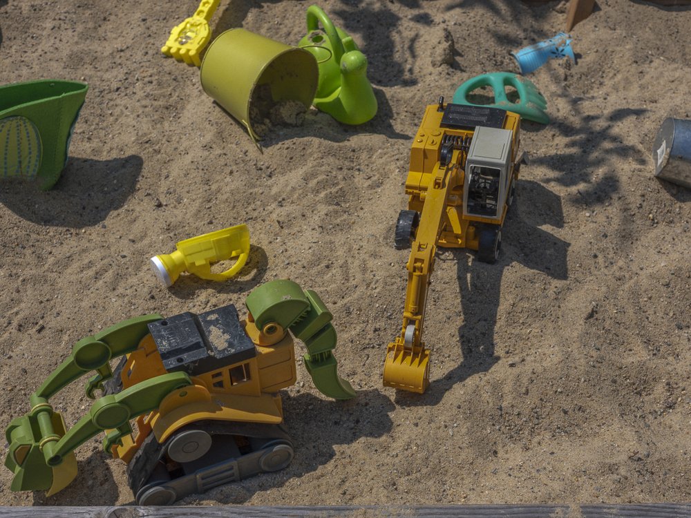 Color photograph looking down on a sandbox with toy excavators, buckets, and watering cans.