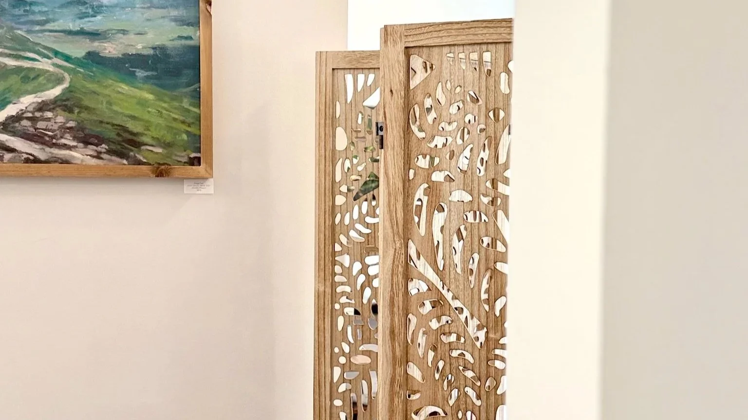 Gallery interior at The Fifth Om in Kennebunk, Maine, with landscape artwork and carved wood screen