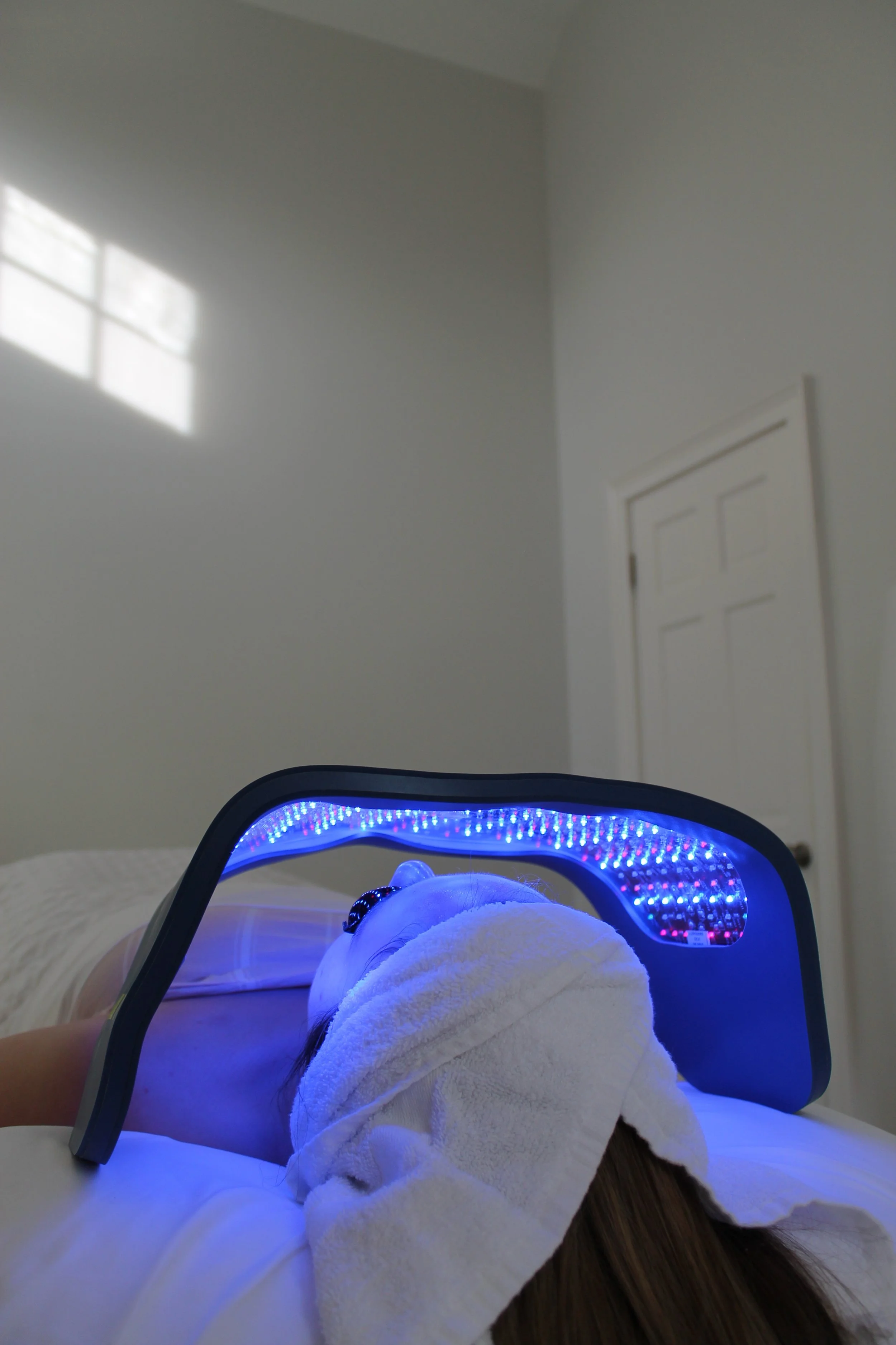LED light therapy panel over woman's face during facial to treat acne, scars, wrinkles