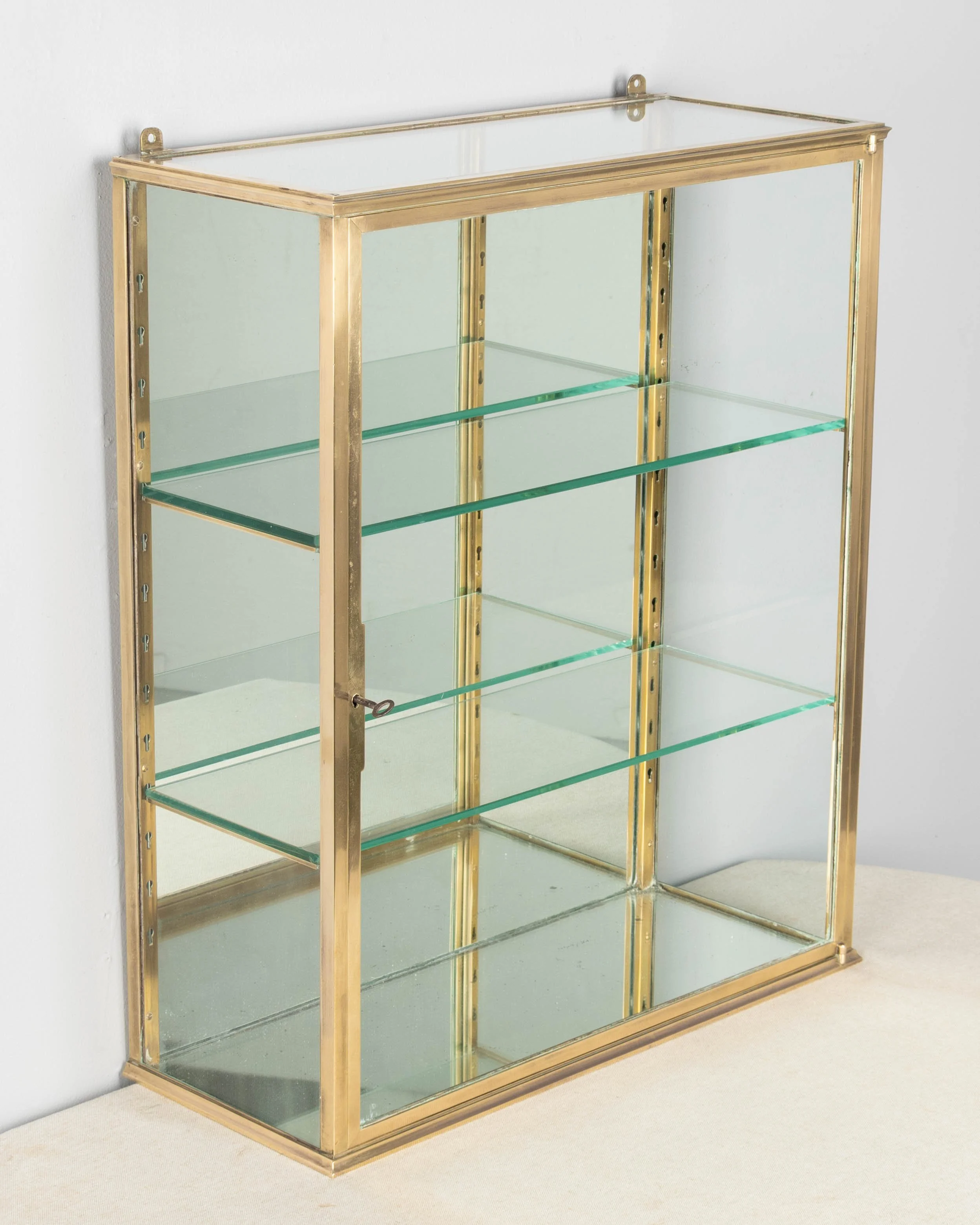 A French Art Deco hanging wall vitrine with solid brass frame, mirrored back and glass panes.