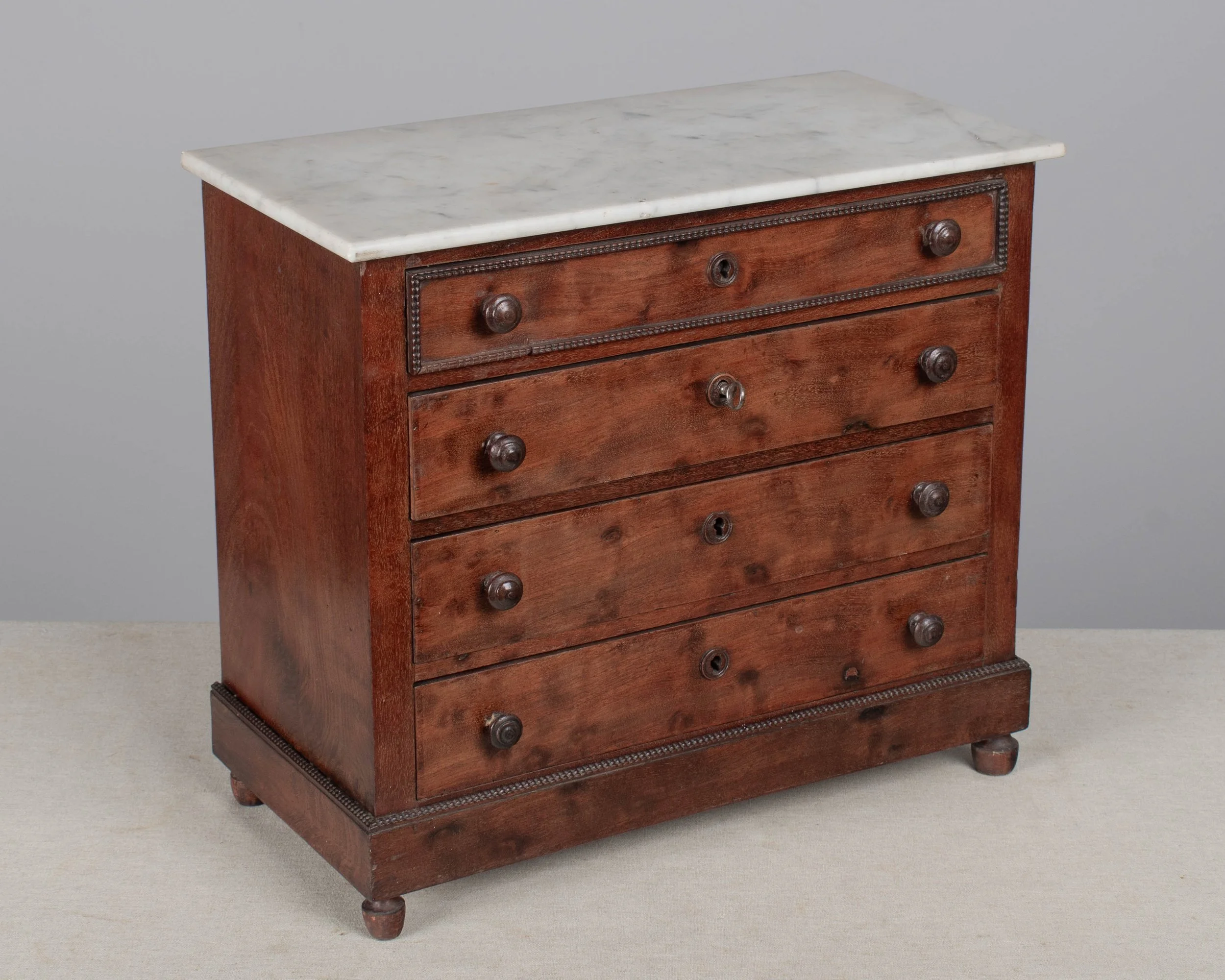 A 19th century Louis Philippe miniature sample commode made of mahogany with French polish finish. Four dovetailed drawers with turned knobs and escutcheons