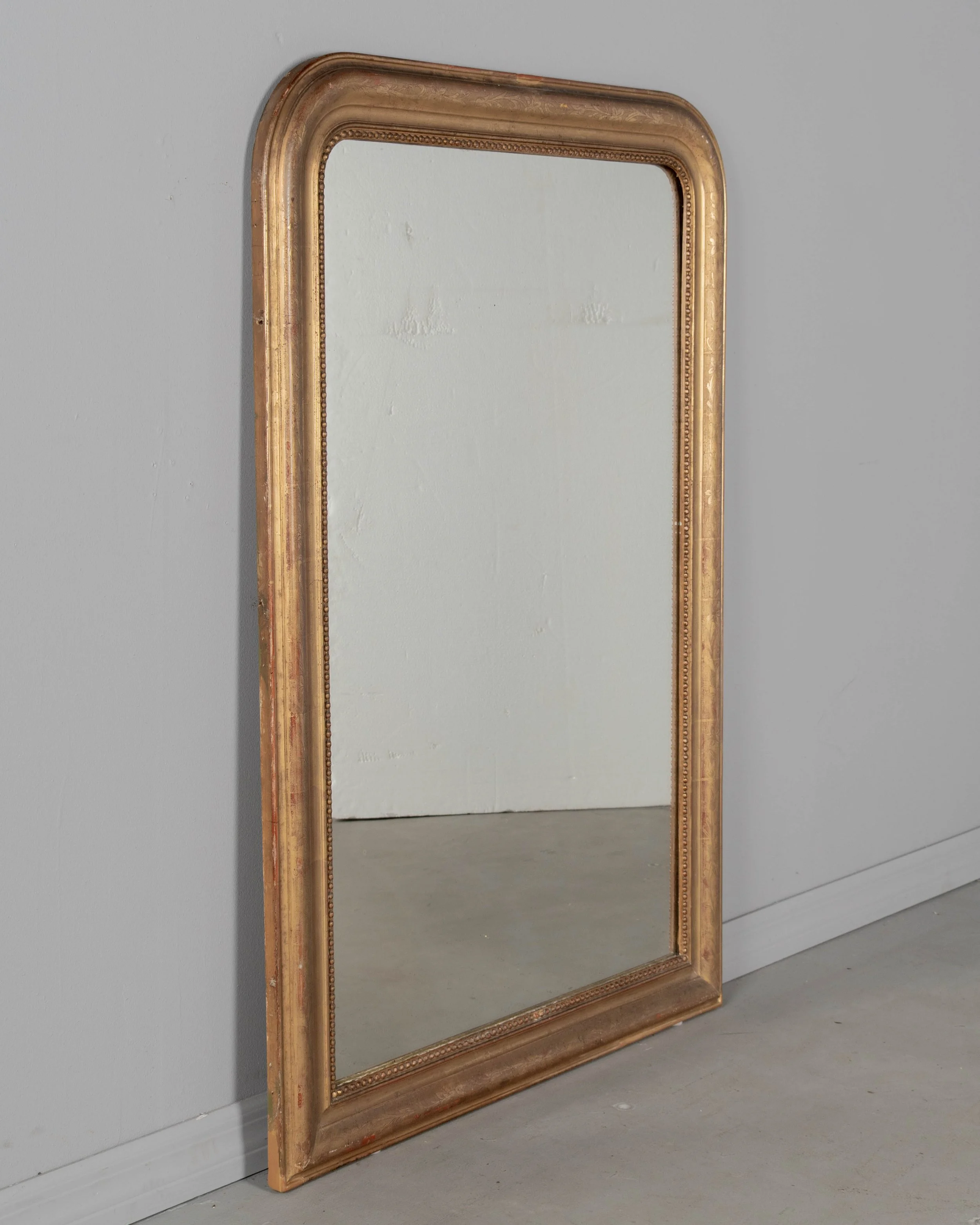 An early 20th century French Louis Philippe style gilded mirror with curved top corners, incised floral decoration and inner bead border.