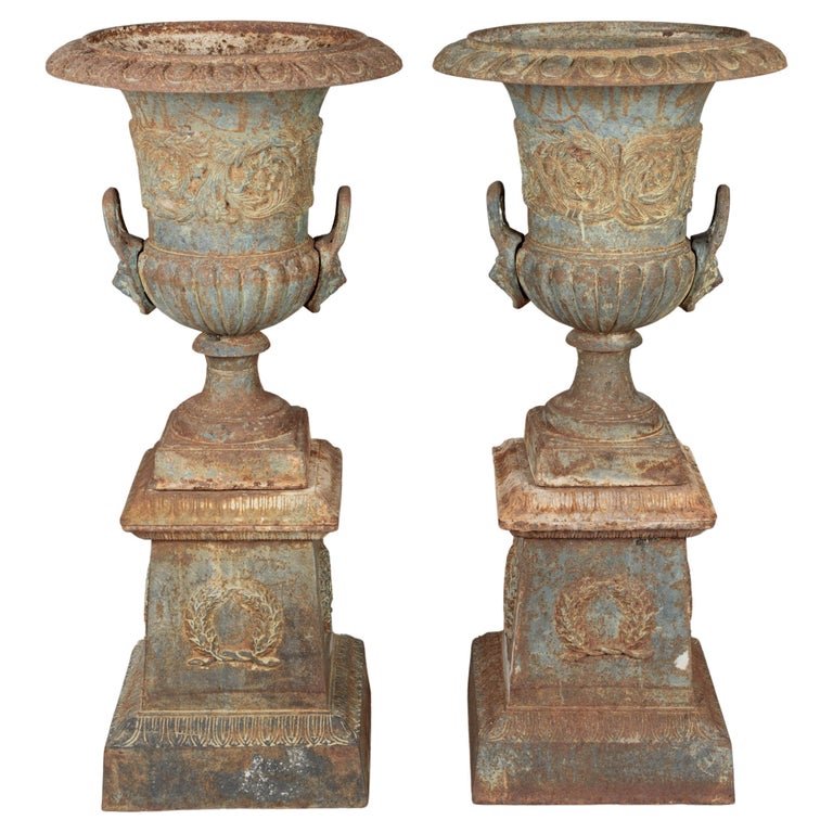 A pair of 19th century French cast iron garden urn planters. In three parts, the tall urn rests on a pedestal base which has a removable rim. Fine cast details with large lion head handles and swirling foliate relief across the face of the urns and l