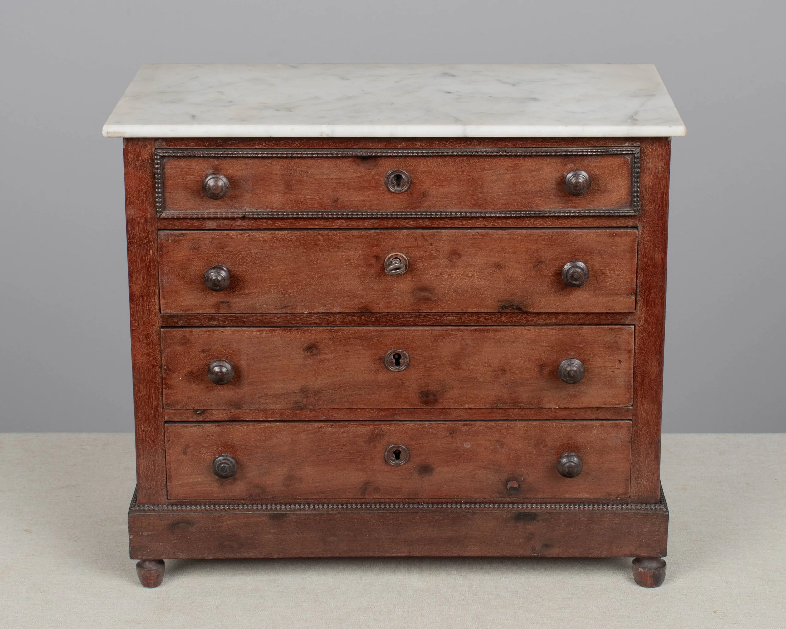 A 19th century Louis Philippe miniature sample commode made of mahogany with French polish finish. Four dovetailed drawers with turned knobs and escutcheons