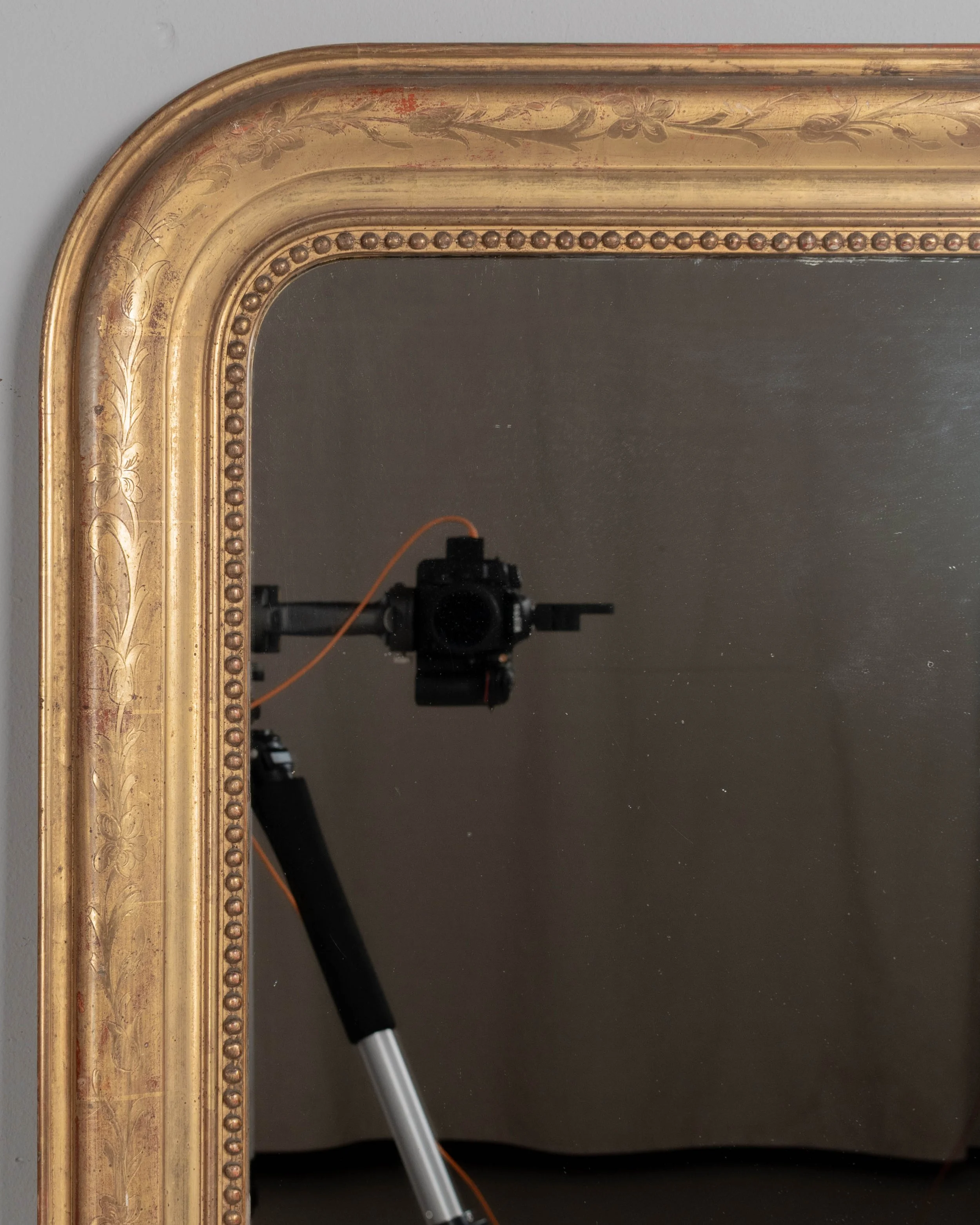 An early 20th century French Louis Philippe style gilded mirror with curved top corners, incised floral decoration and inner bead border.