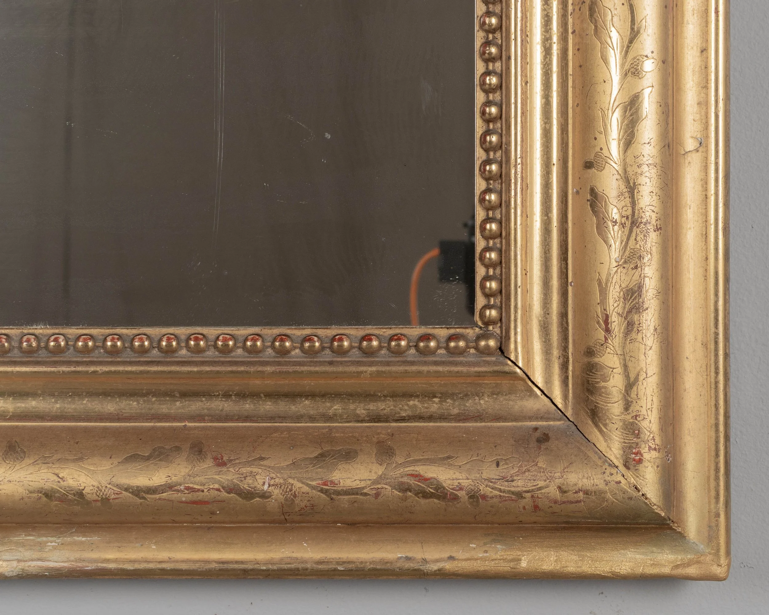 An early 20th century French Louis Philippe style gilded mirror with curved top corners, incised floral decoration and inner bead border.