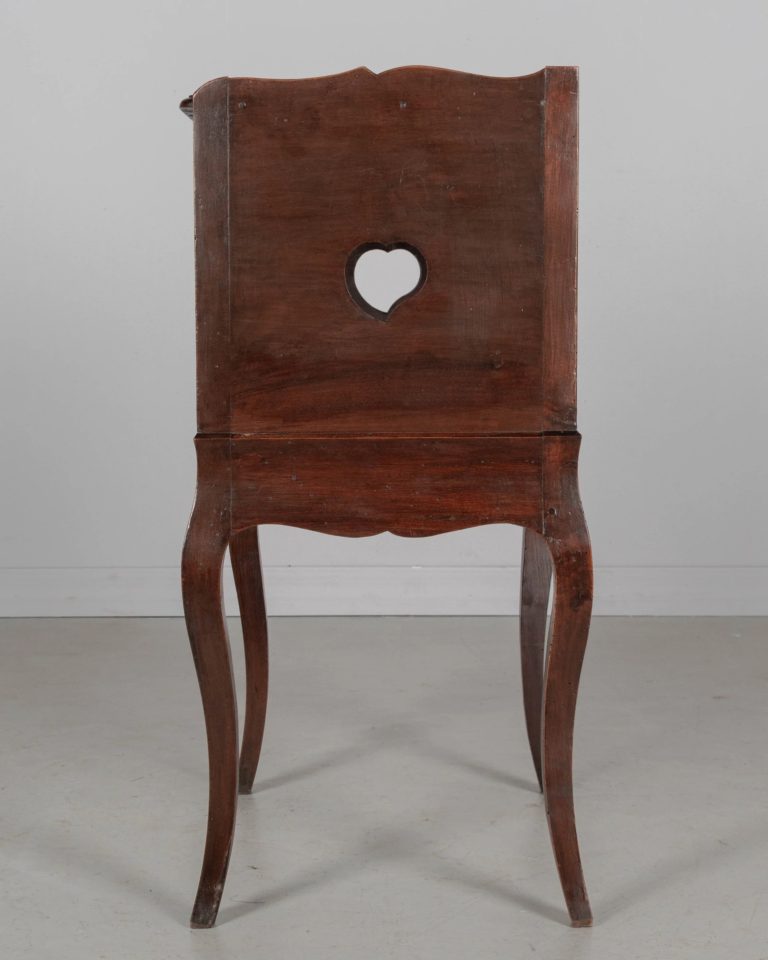 An early 20th century Louis XV Country French side table or nightstand made of solid walnut with an open niche and pierced heart shaped cut-outs on the sides.