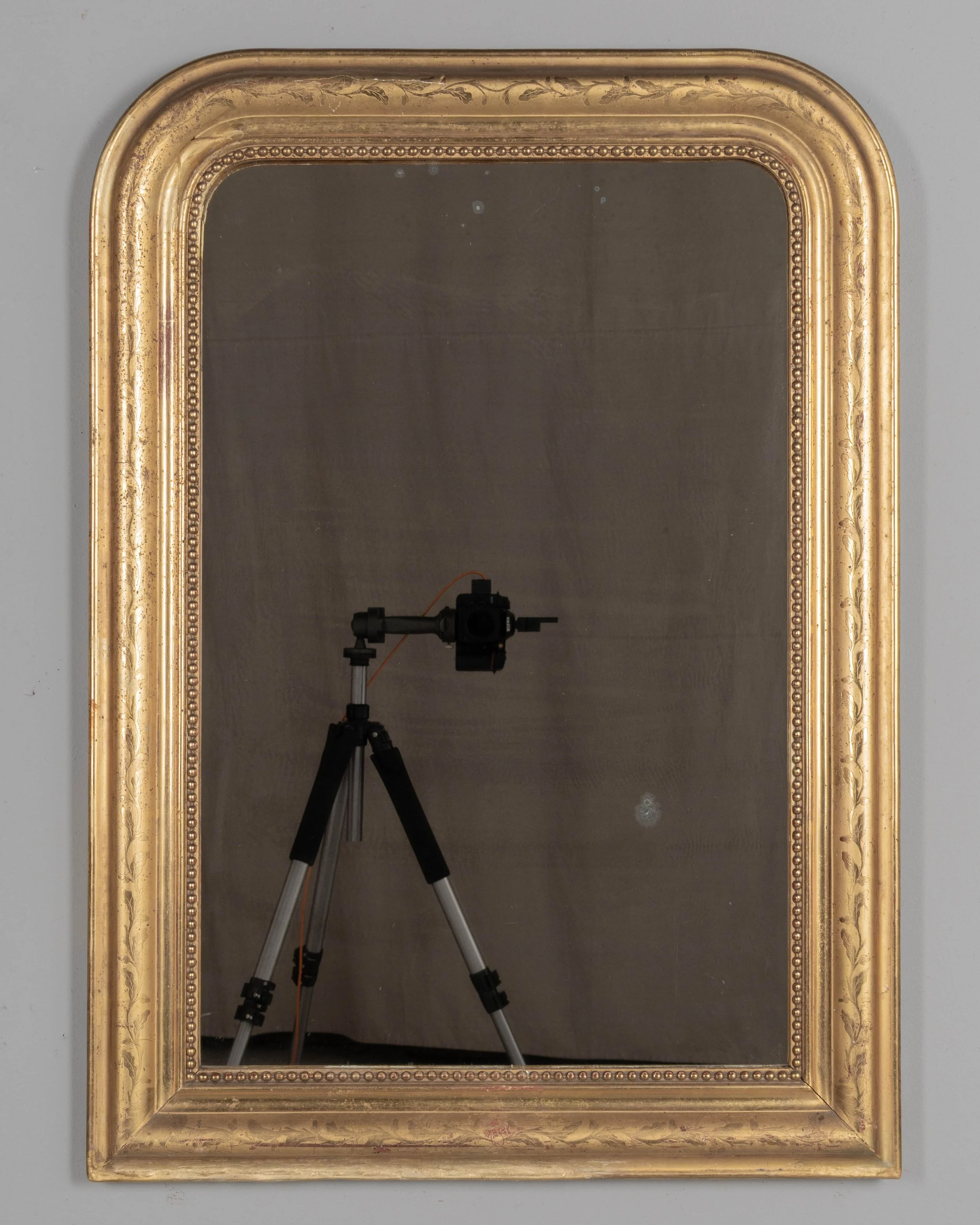 An early 20th century French Louis Philippe style gilded mirror with curved top corners, incised floral decoration and inner bead border.