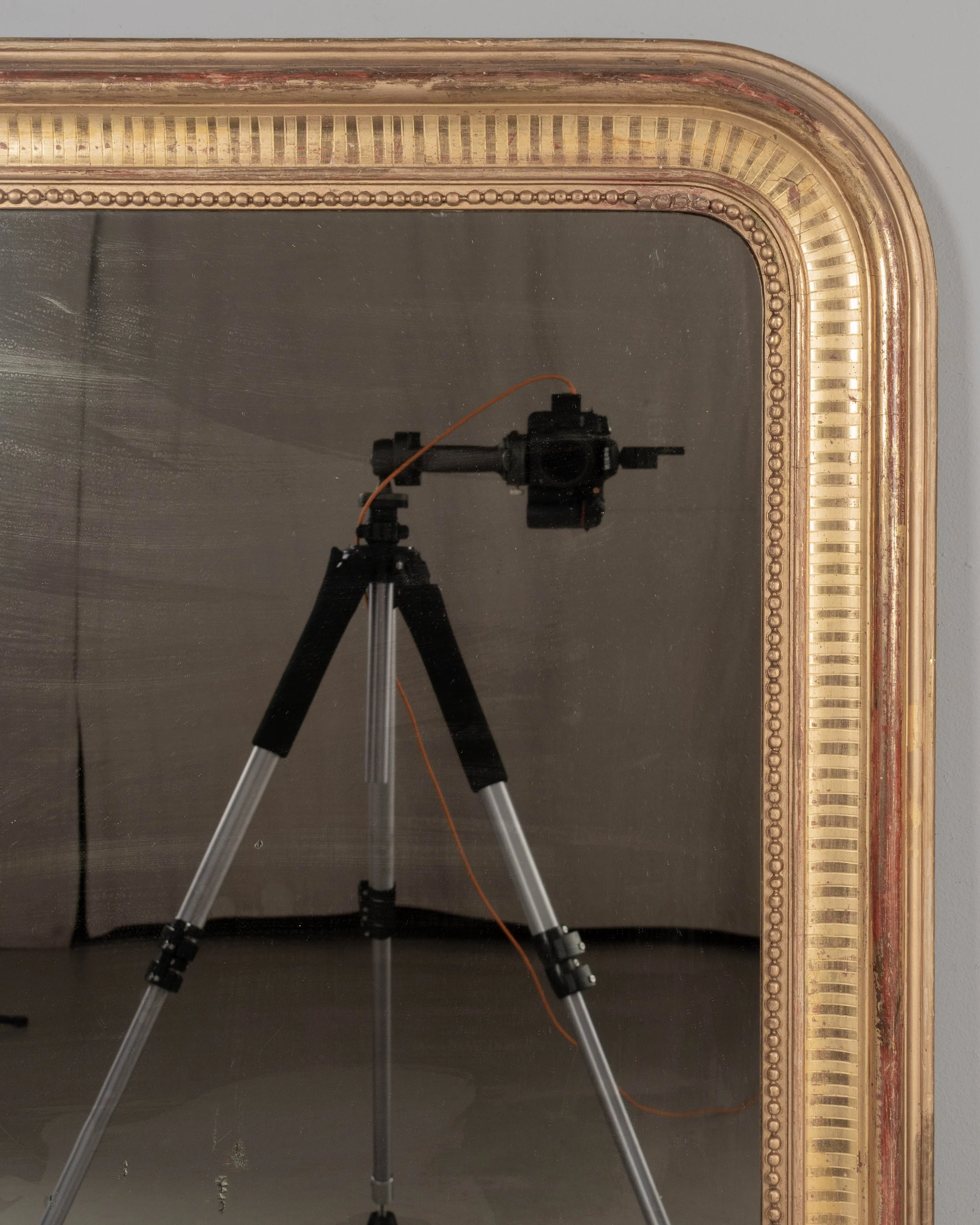 A 19th century French Louis Philippe style gilded mirror with curved top corners, incised ribbed decoration and inner bead border. Warm gilt finish with red under rub exposed.