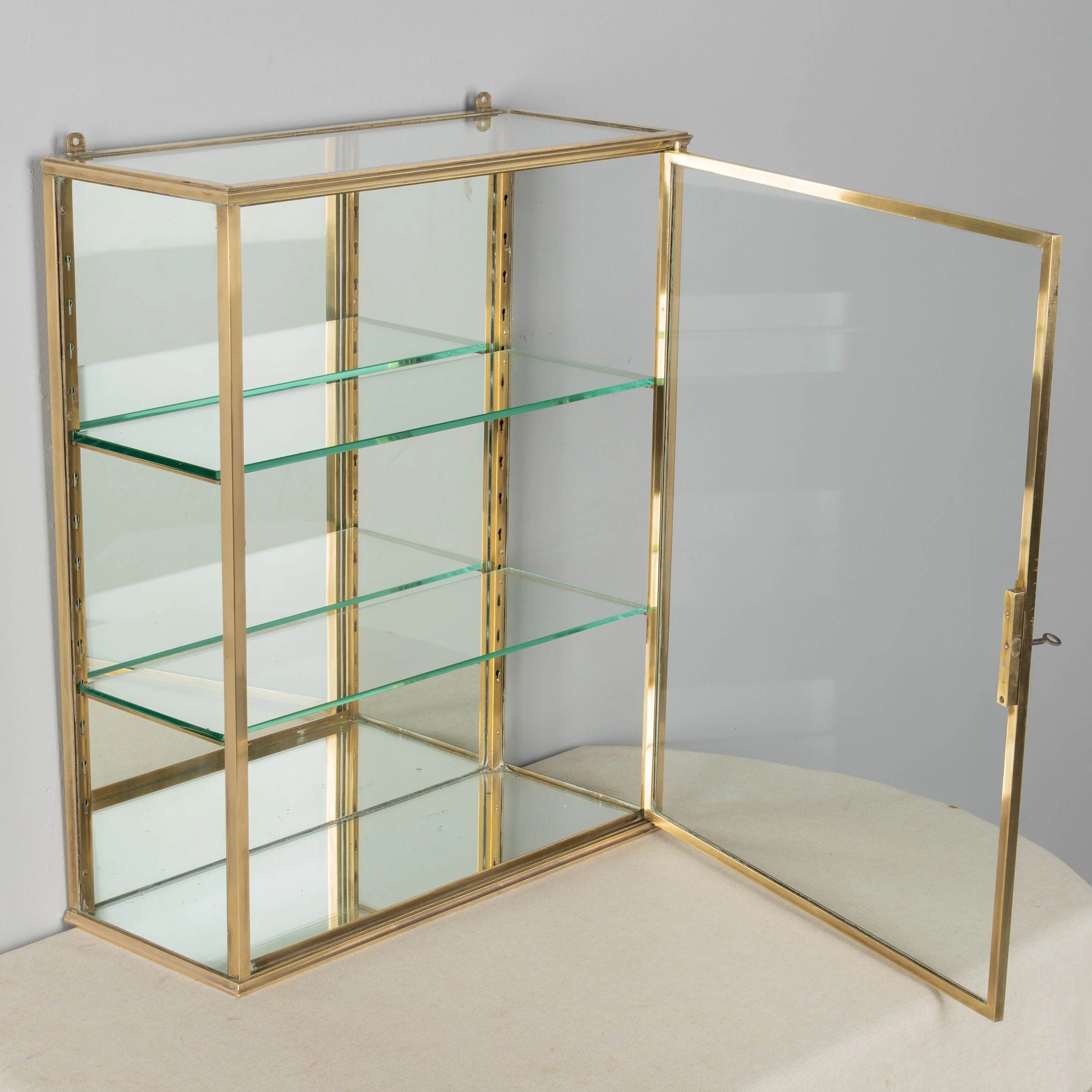A French Art Deco hanging wall vitrine with solid brass frame, mirrored back and glass panes.