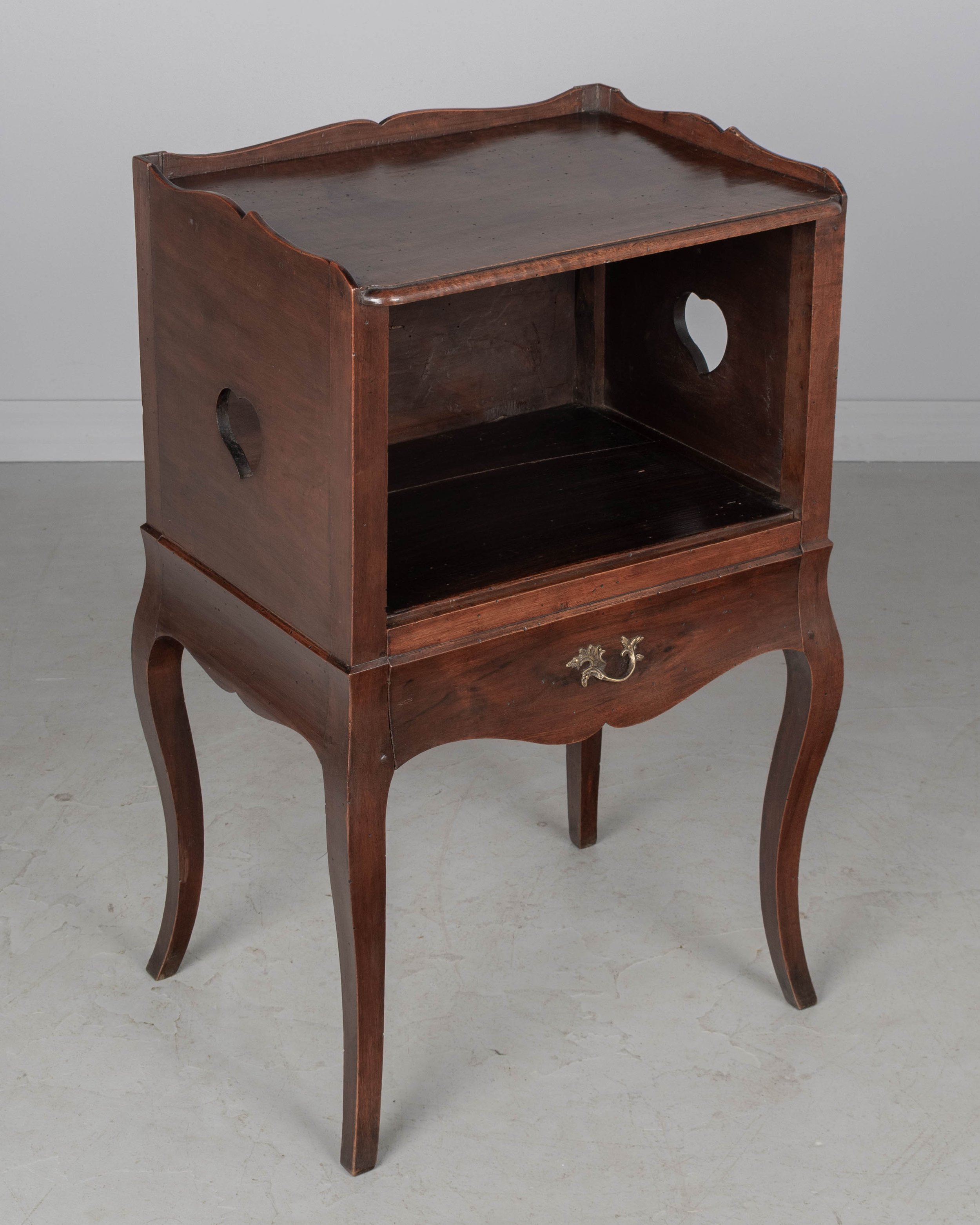 An early 20th century Louis XV Country French side table or nightstand made of solid walnut with an open niche and pierced heart shaped cut-outs on the sides.