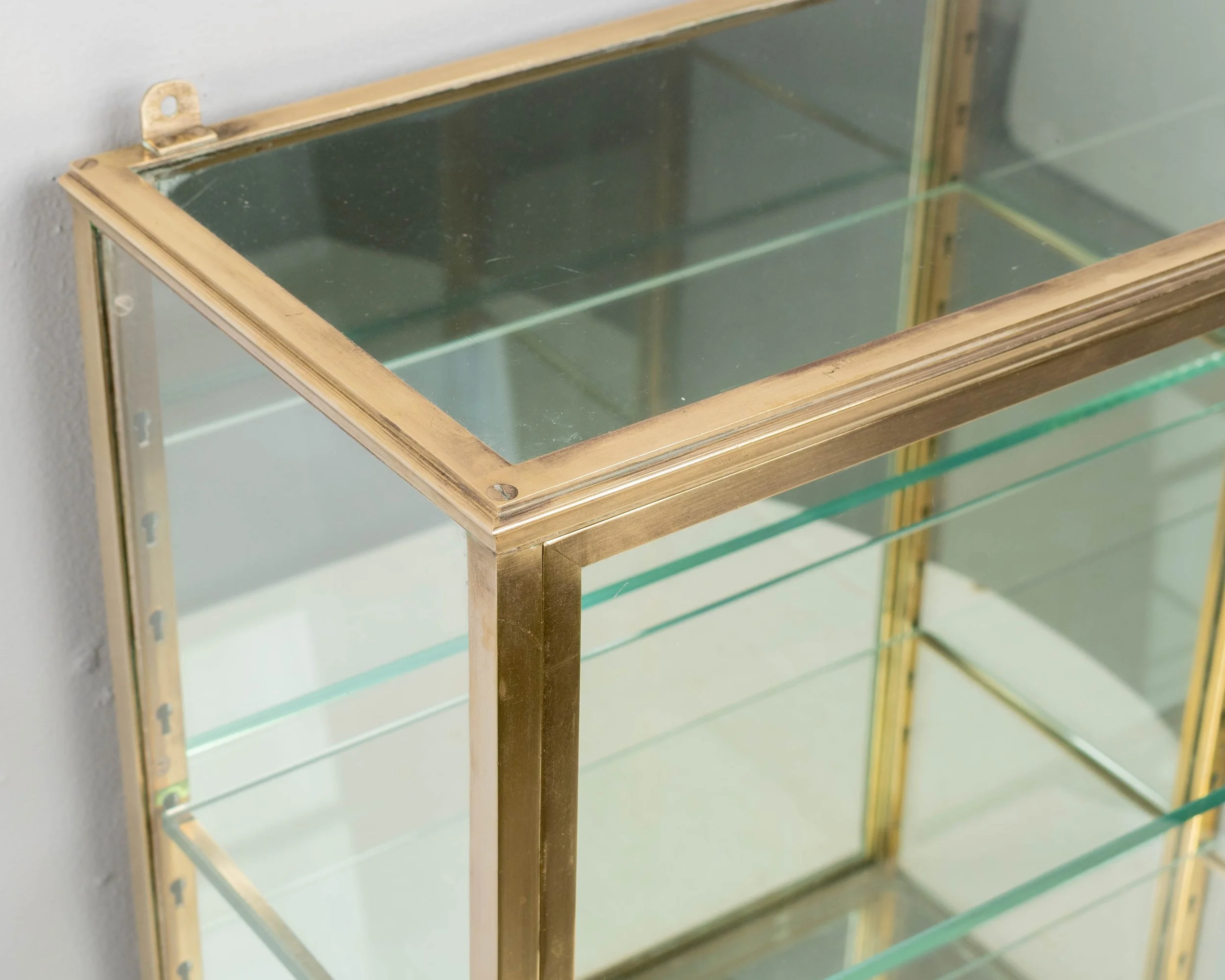 A French Art Deco hanging wall vitrine with solid brass frame, mirrored back and glass panes.