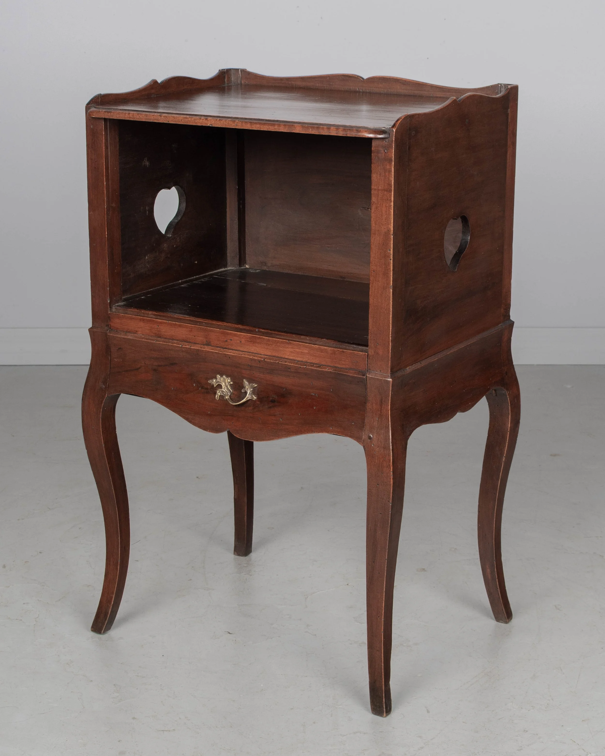 An early 20th century Louis XV Country French side table or nightstand made of solid walnut with an open niche and pierced heart shaped cut-outs on the sides.