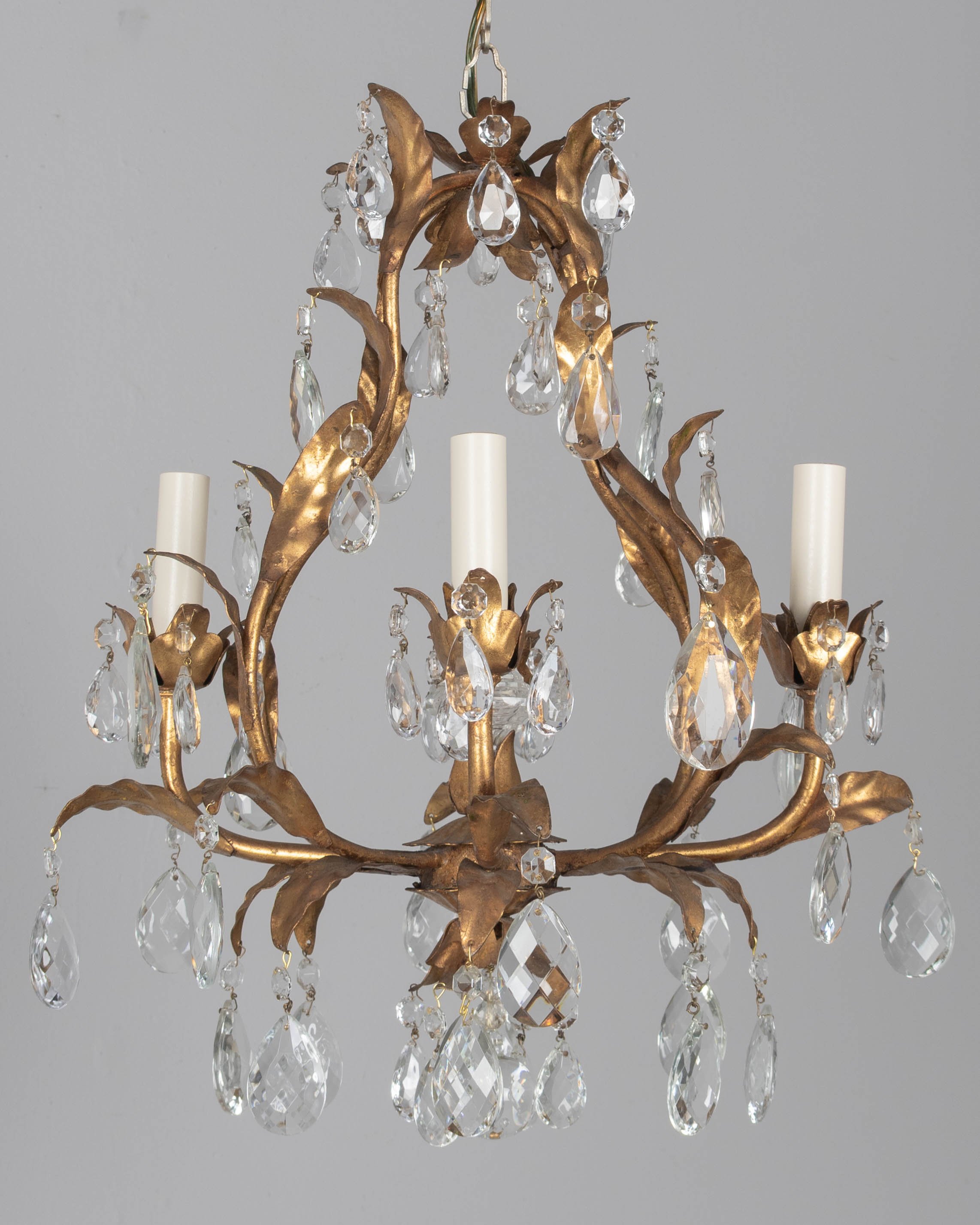An Italian Hollywood Regency style four-light gilt metal chandelier with tôle leaves and crystal prisms.