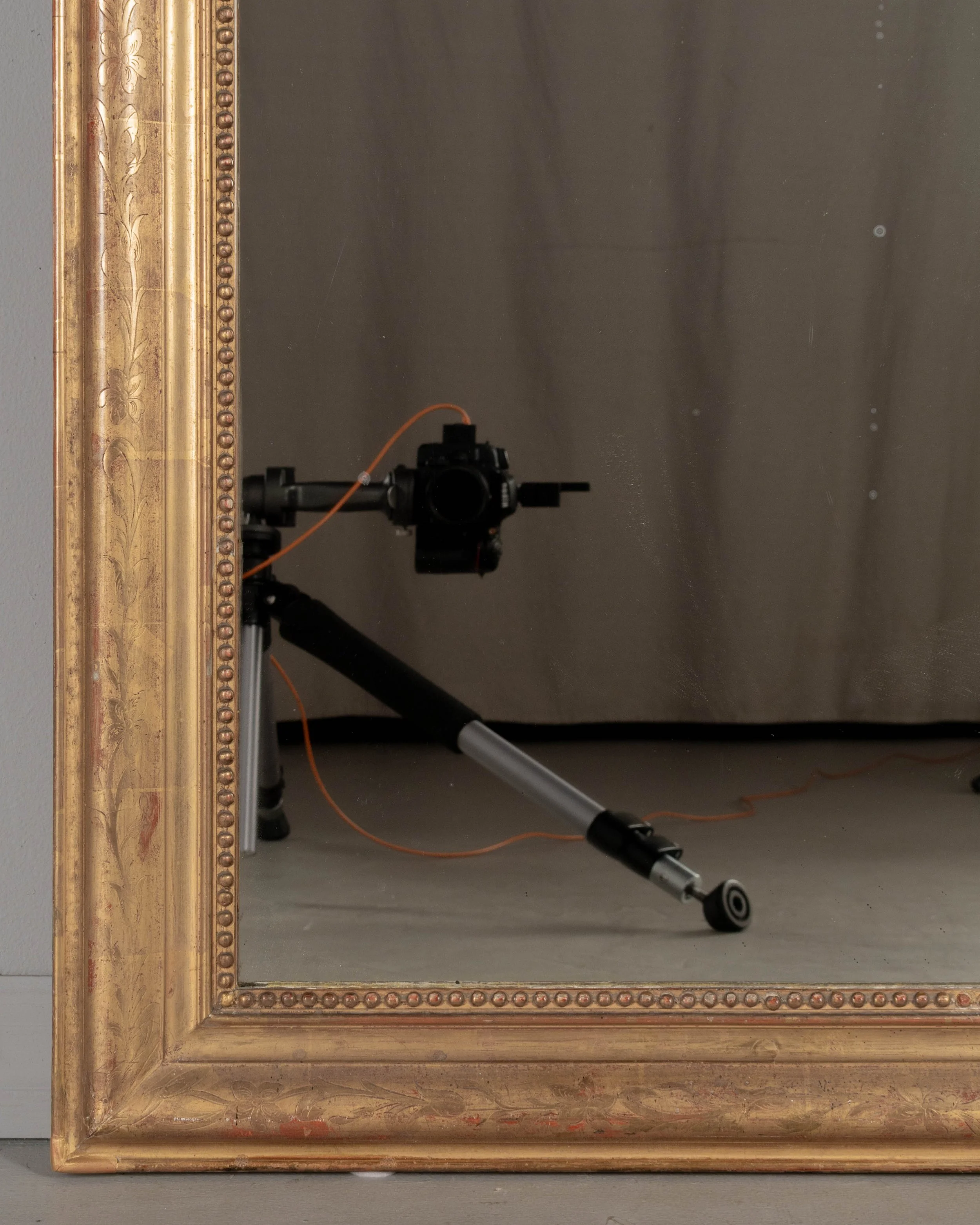 An early 20th century French Louis Philippe style gilded mirror with curved top corners, incised floral decoration and inner bead border.