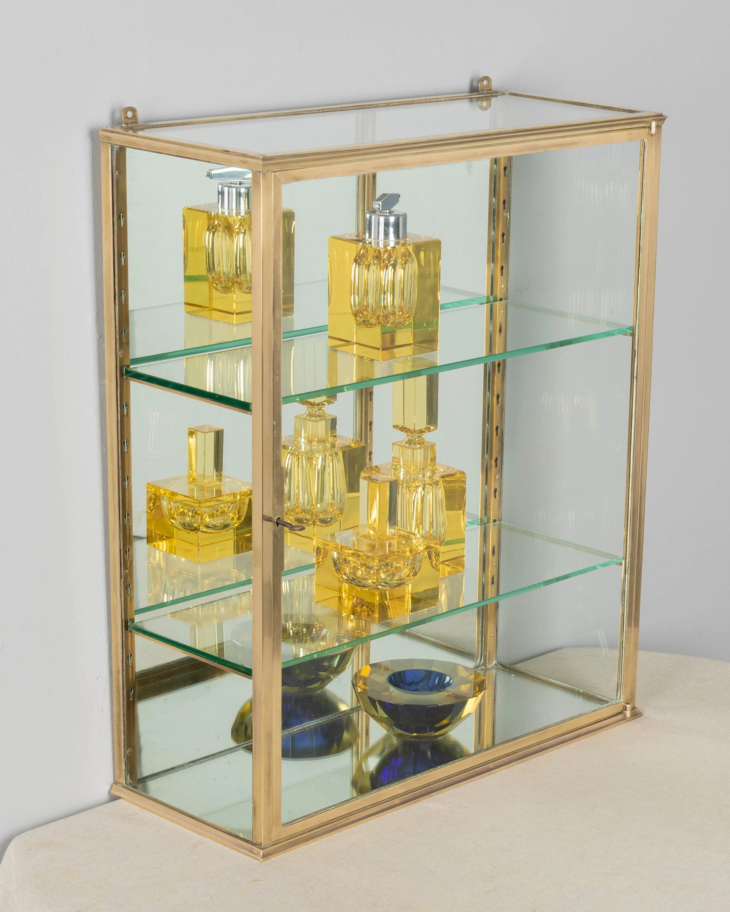 A French Art Deco hanging wall vitrine with solid brass frame, mirrored back and glass panes.