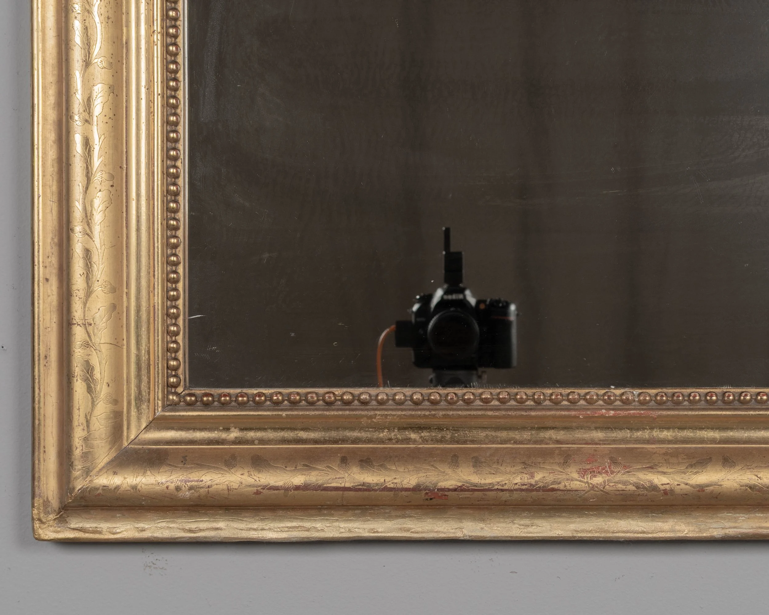 An early 20th century French Louis Philippe style gilded mirror with curved top corners, incised floral decoration and inner bead border.