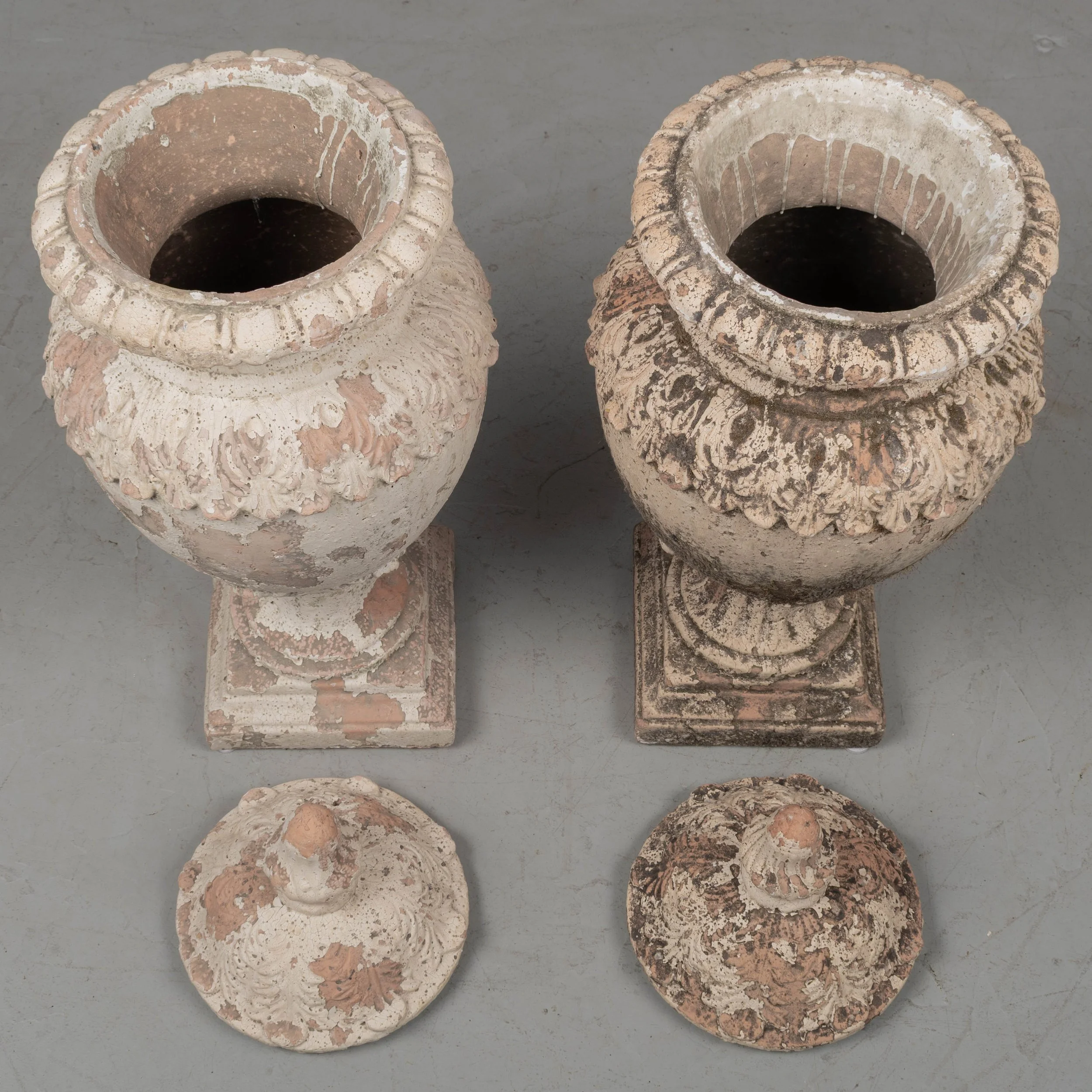 A pair of French terracotta garden urns with lids. Classical vase form on pedestal base, decorated in acanthus leaf motif with large acorn finials on lids.