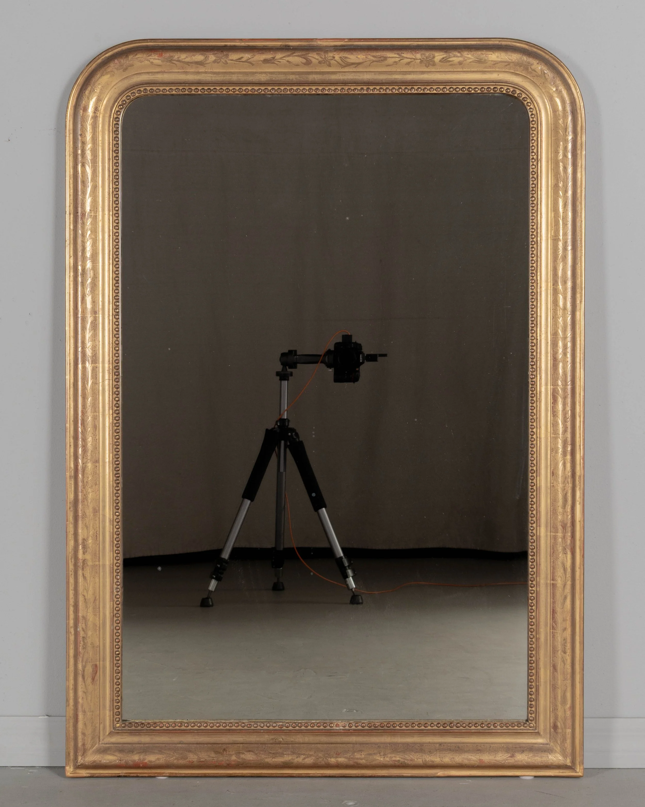 An early 20th century French Louis Philippe style gilded mirror with curved top corners, incised floral decoration and inner bead border.