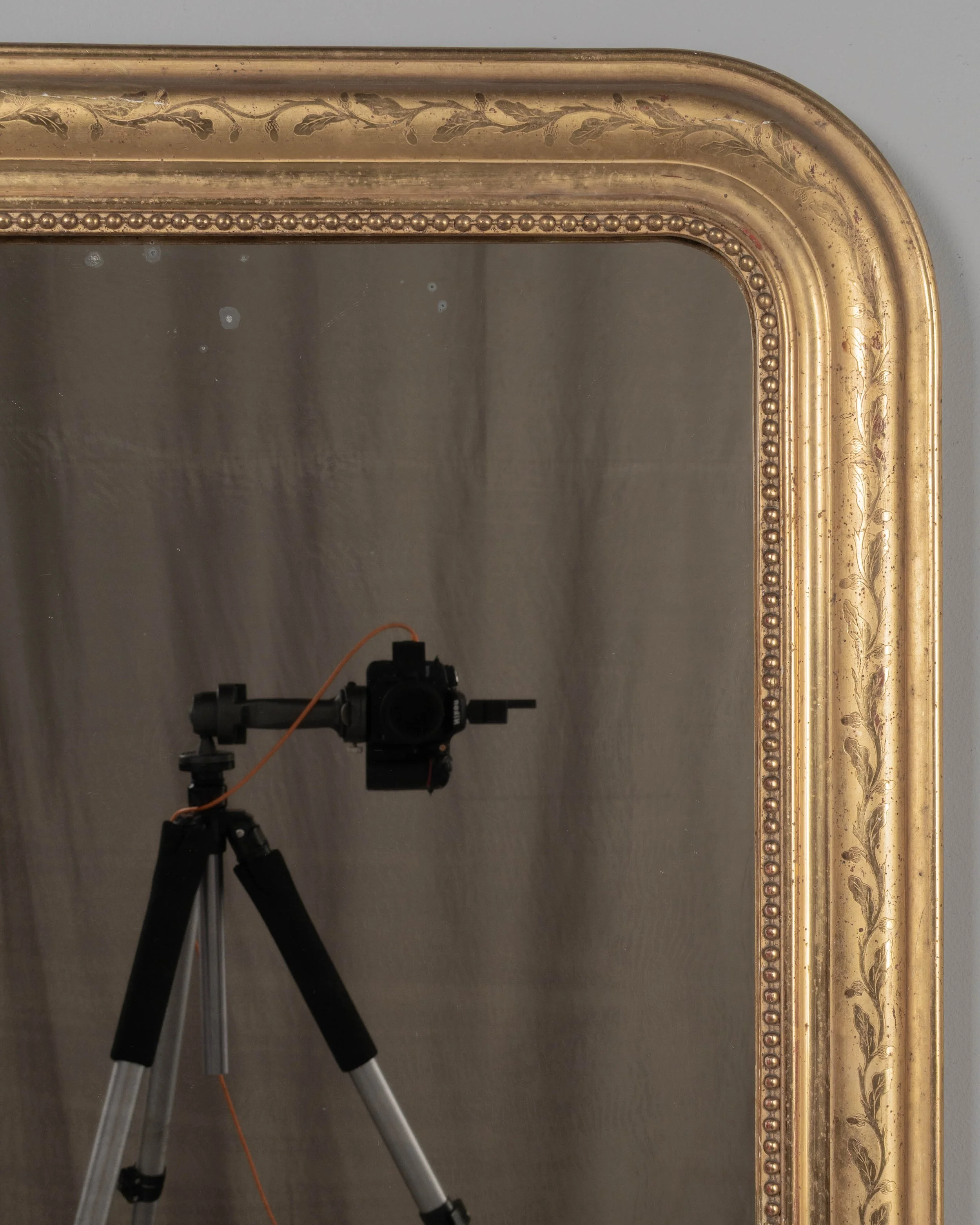 An early 20th century French Louis Philippe style gilded mirror with curved top corners, incised floral decoration and inner bead border.