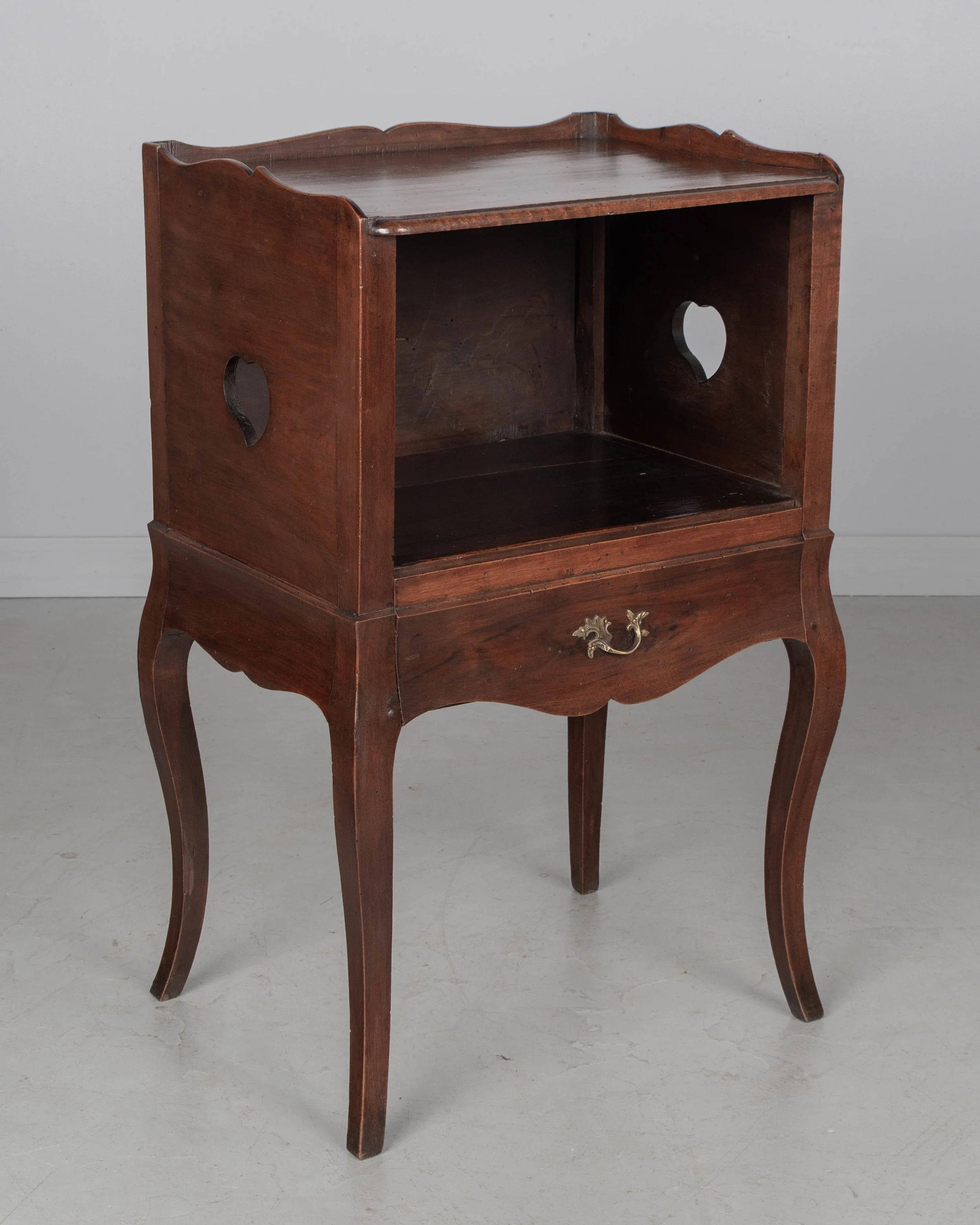 An early 20th century Louis XV Country French side table or nightstand made of solid walnut with an open niche and pierced heart shaped cut-outs on the sides.