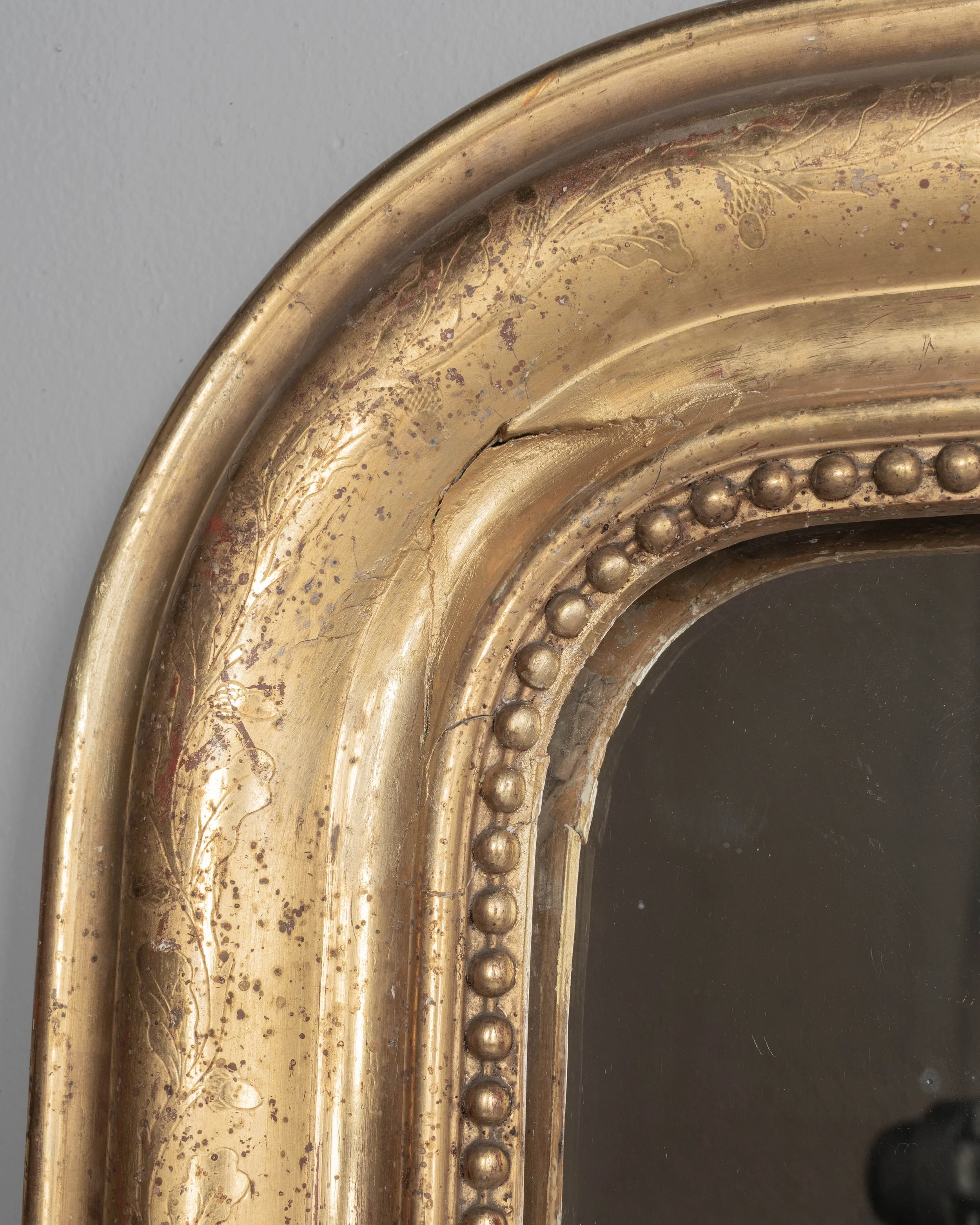 An early 20th century French Louis Philippe style gilded mirror with curved top corners, incised floral decoration and inner bead border.