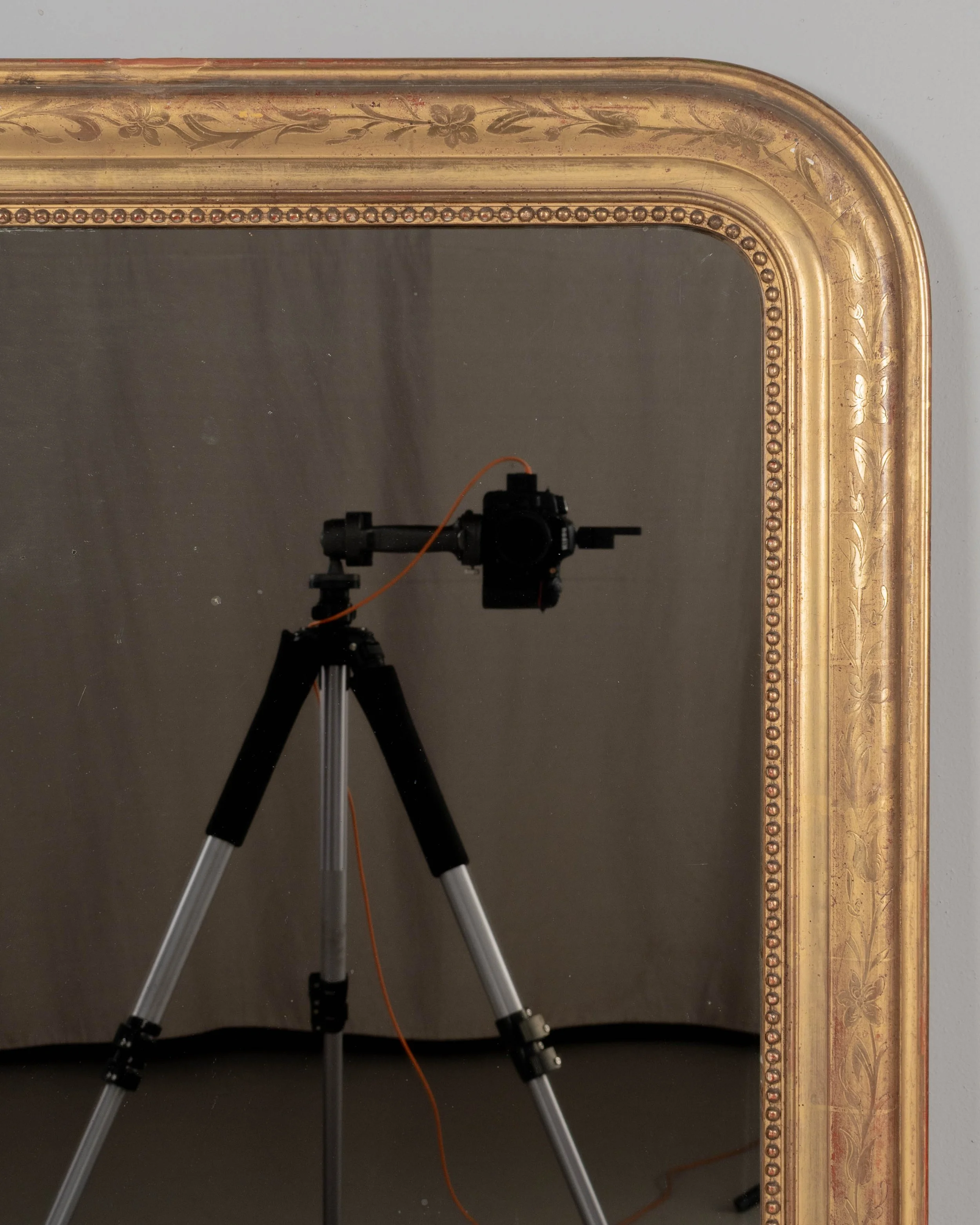 An early 20th century French Louis Philippe style gilded mirror with curved top corners, incised floral decoration and inner bead border.