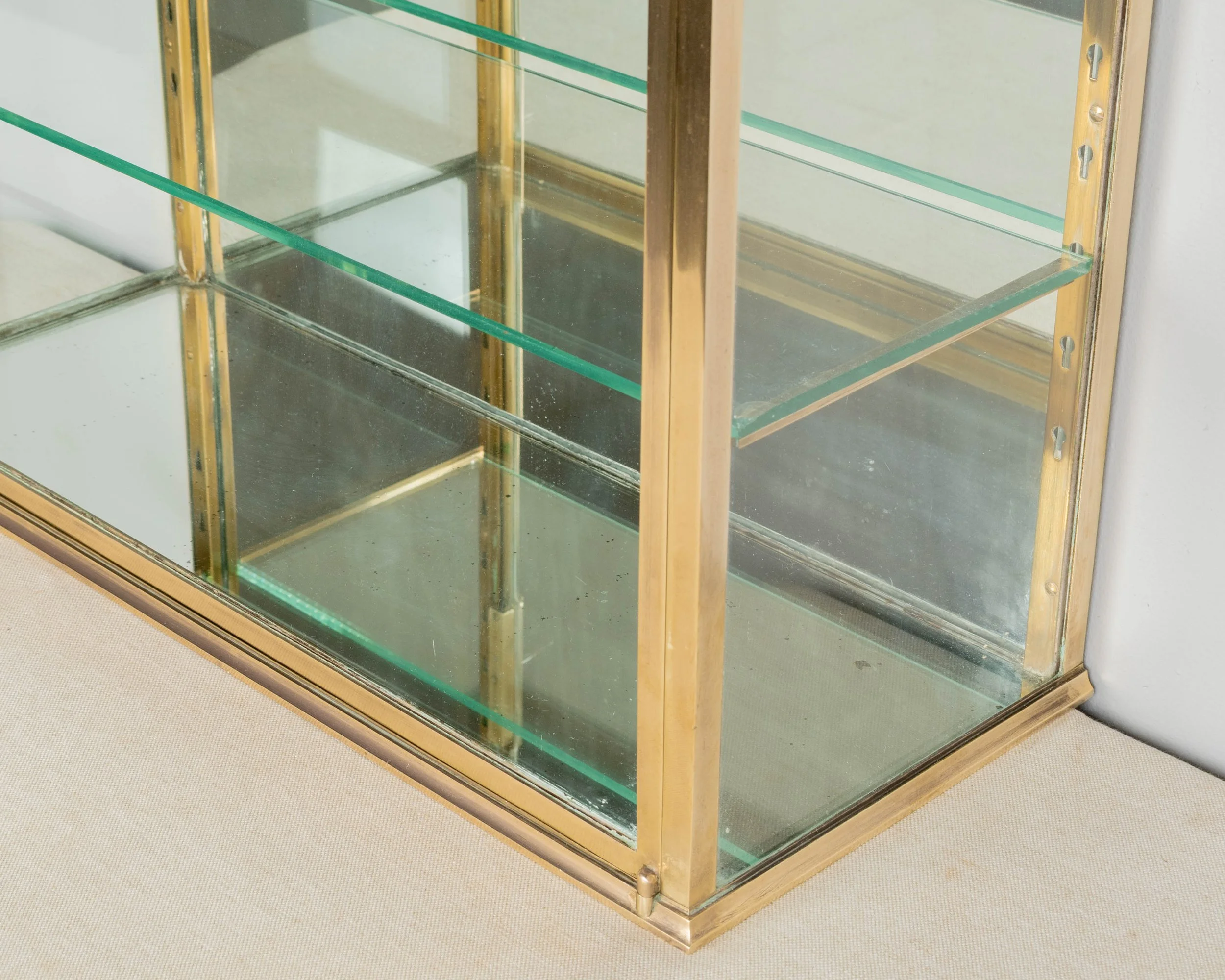A French Art Deco hanging wall vitrine with solid brass frame, mirrored back and glass panes.