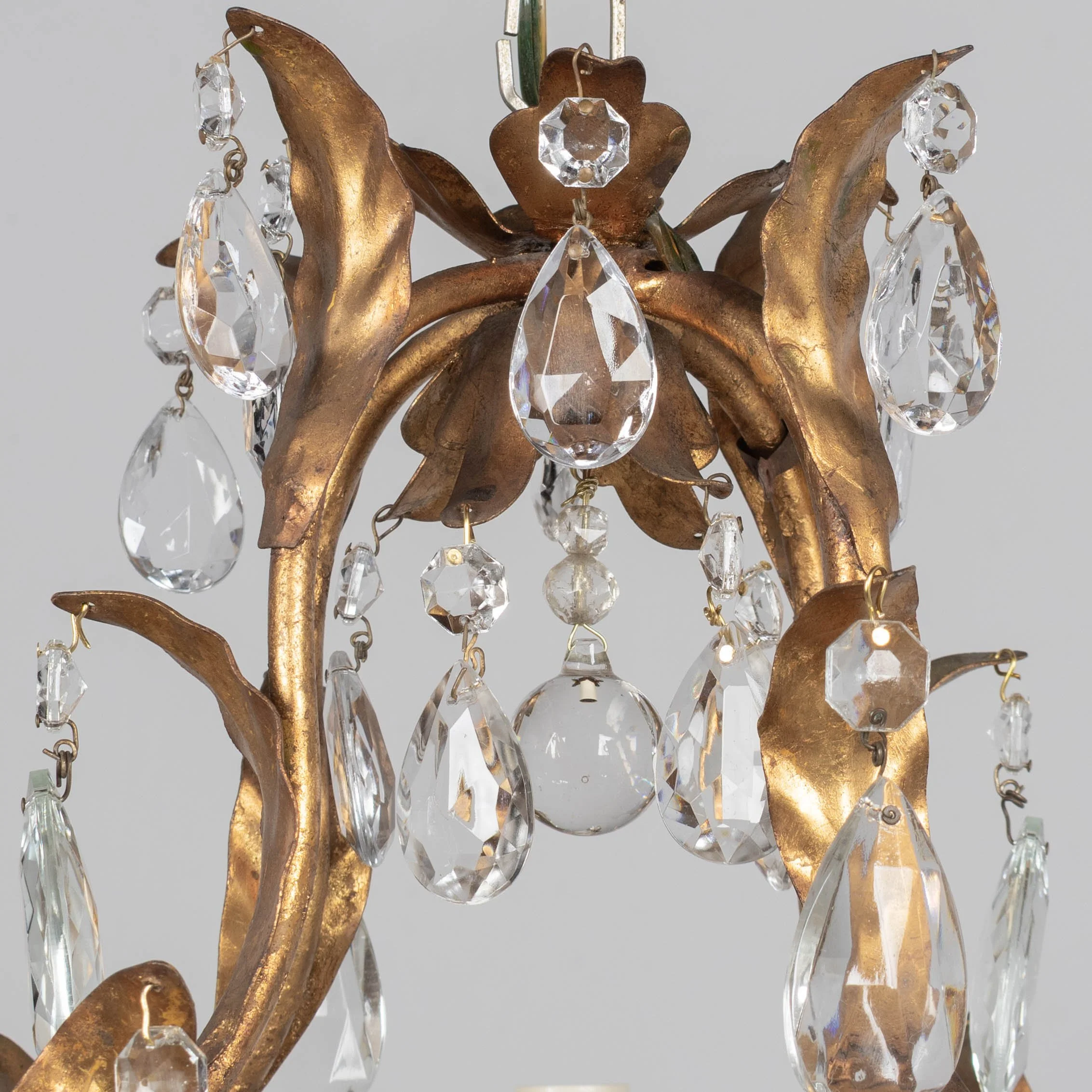 An Italian Hollywood Regency style four-light gilt metal chandelier with tôle leaves and crystal prisms.