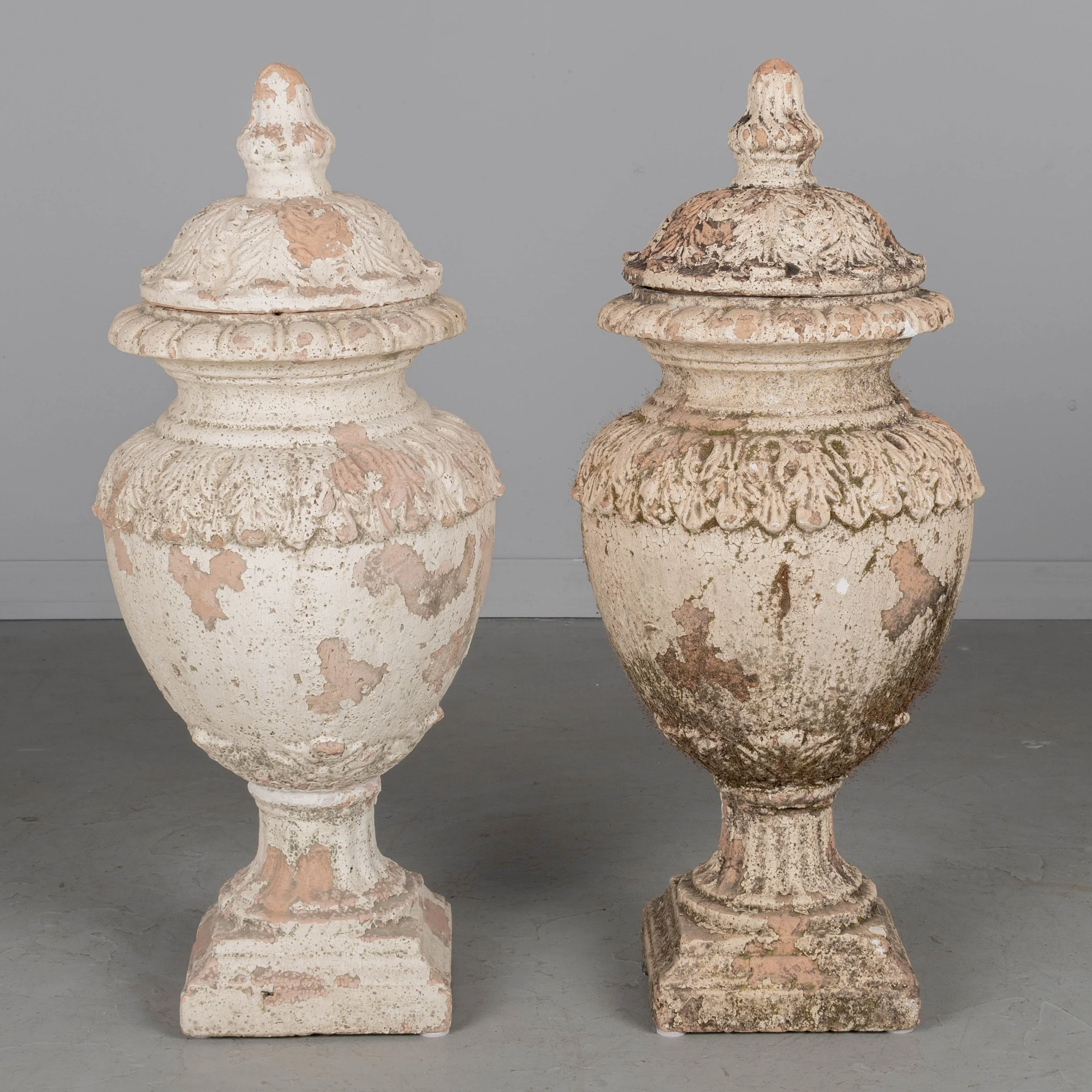 A pair of French terracotta garden urns with lids. Classical vase form on pedestal base, decorated in acanthus leaf motif with large acorn finials on lids.