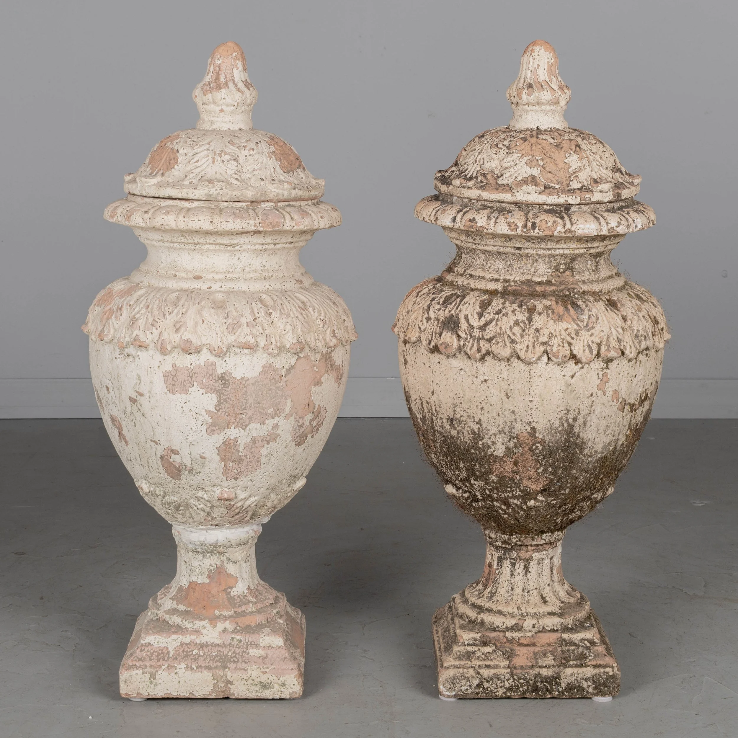 A pair of French terracotta garden urns with lids. Classical vase form on pedestal base, decorated in acanthus leaf motif with large acorn finials on lids.