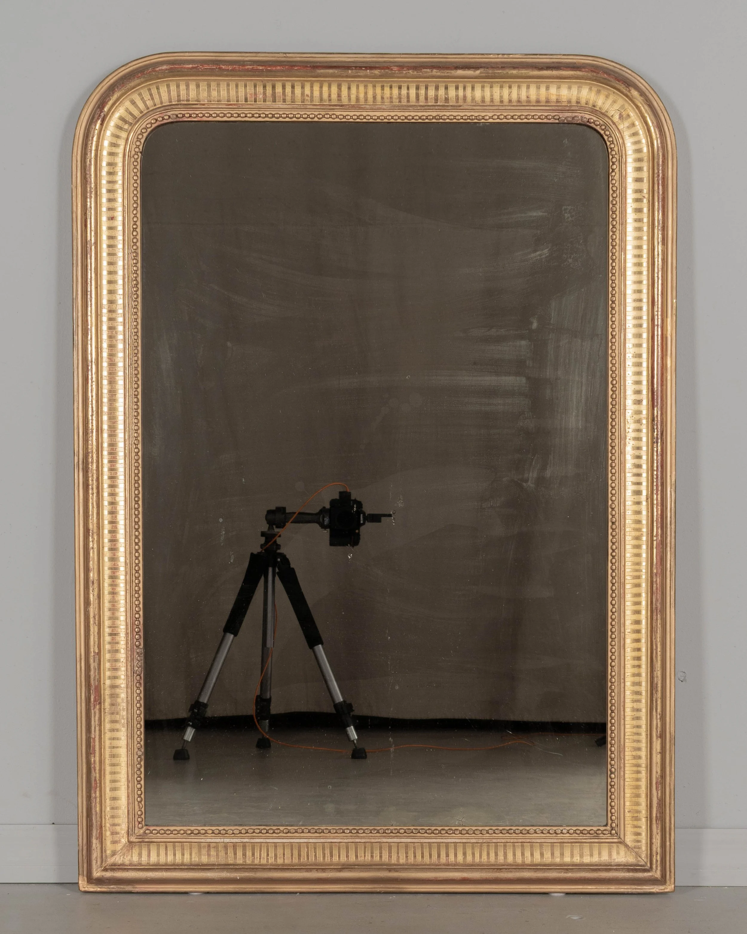 A 19th century French Louis Philippe style gilded mirror with curved top corners, incised ribbed decoration and inner bead border. Warm gilt finish with red under rub exposed.