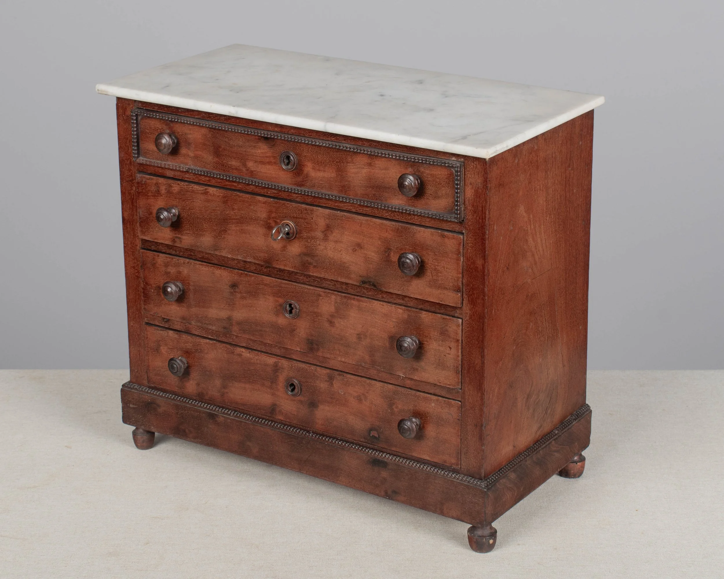 A 19th century Louis Philippe miniature sample commode made of mahogany with French polish finish. Four dovetailed drawers with turned knobs and escutcheons