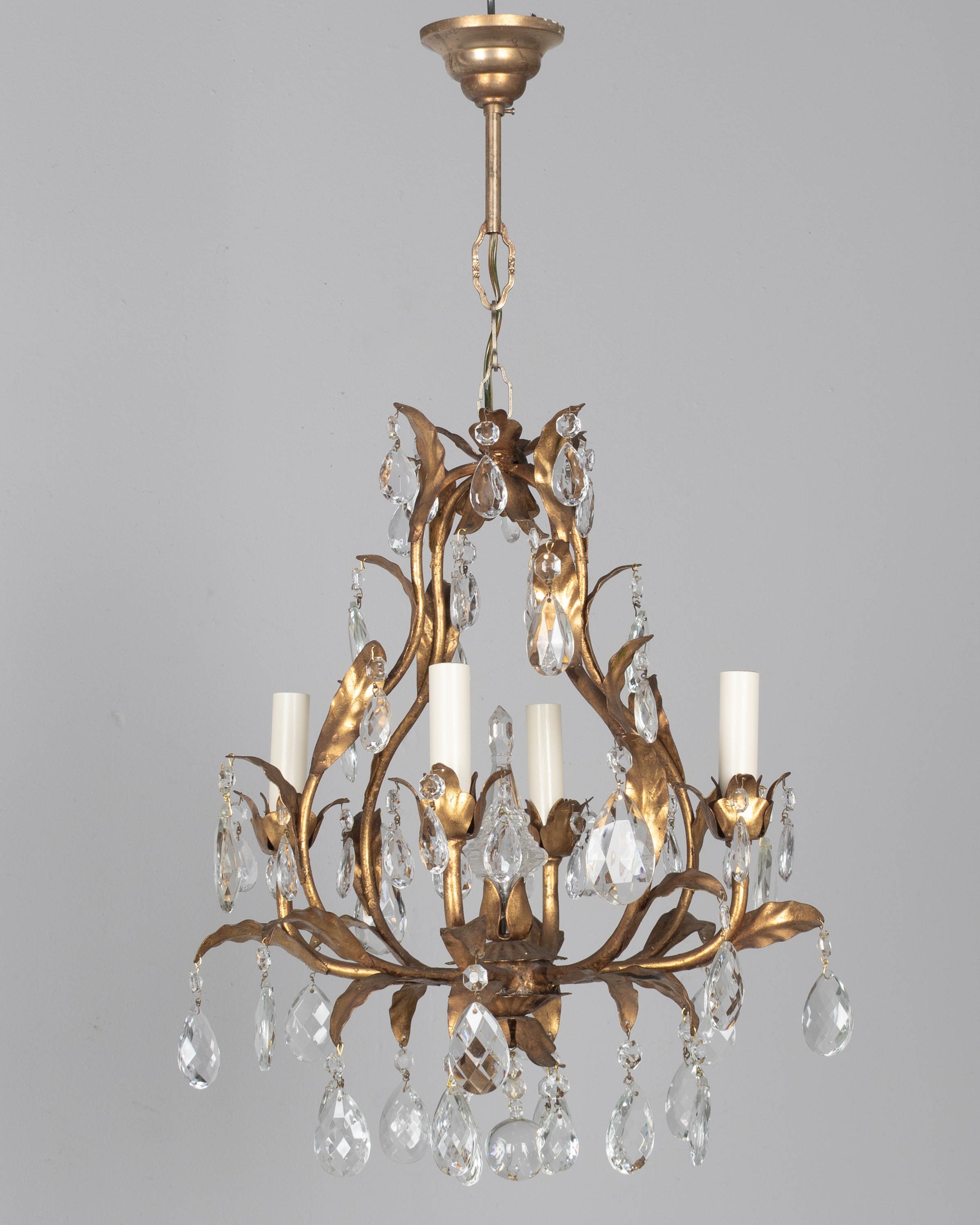 An Italian Hollywood Regency style four-light gilt metal chandelier with tôle leaves and crystal prisms.